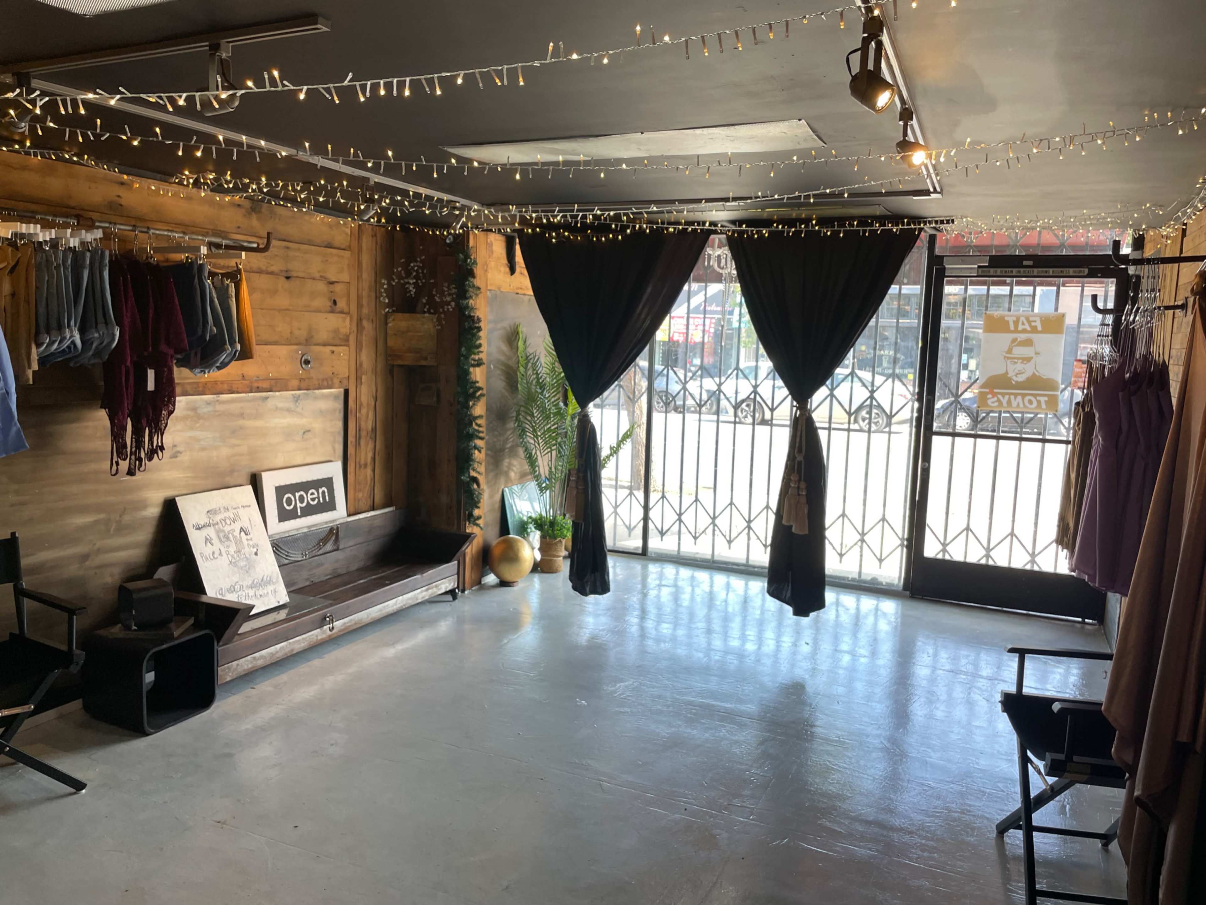 The image shows an empty boutique with wooden walls, string lights, and open curtains leading to a street view.