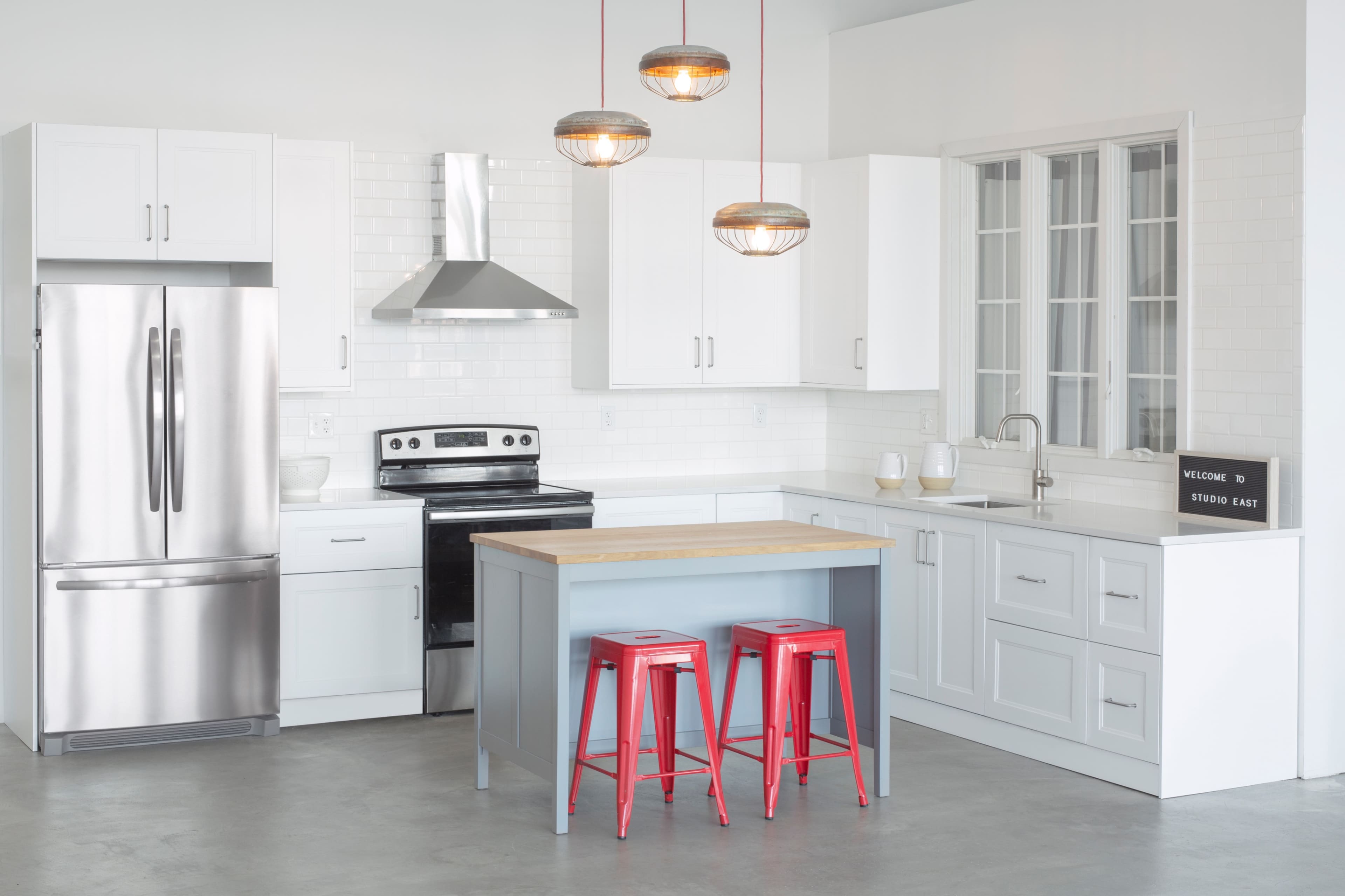 A modern kitchen features white cabinetry, stainless steel appliances, and a central island with red stools.
