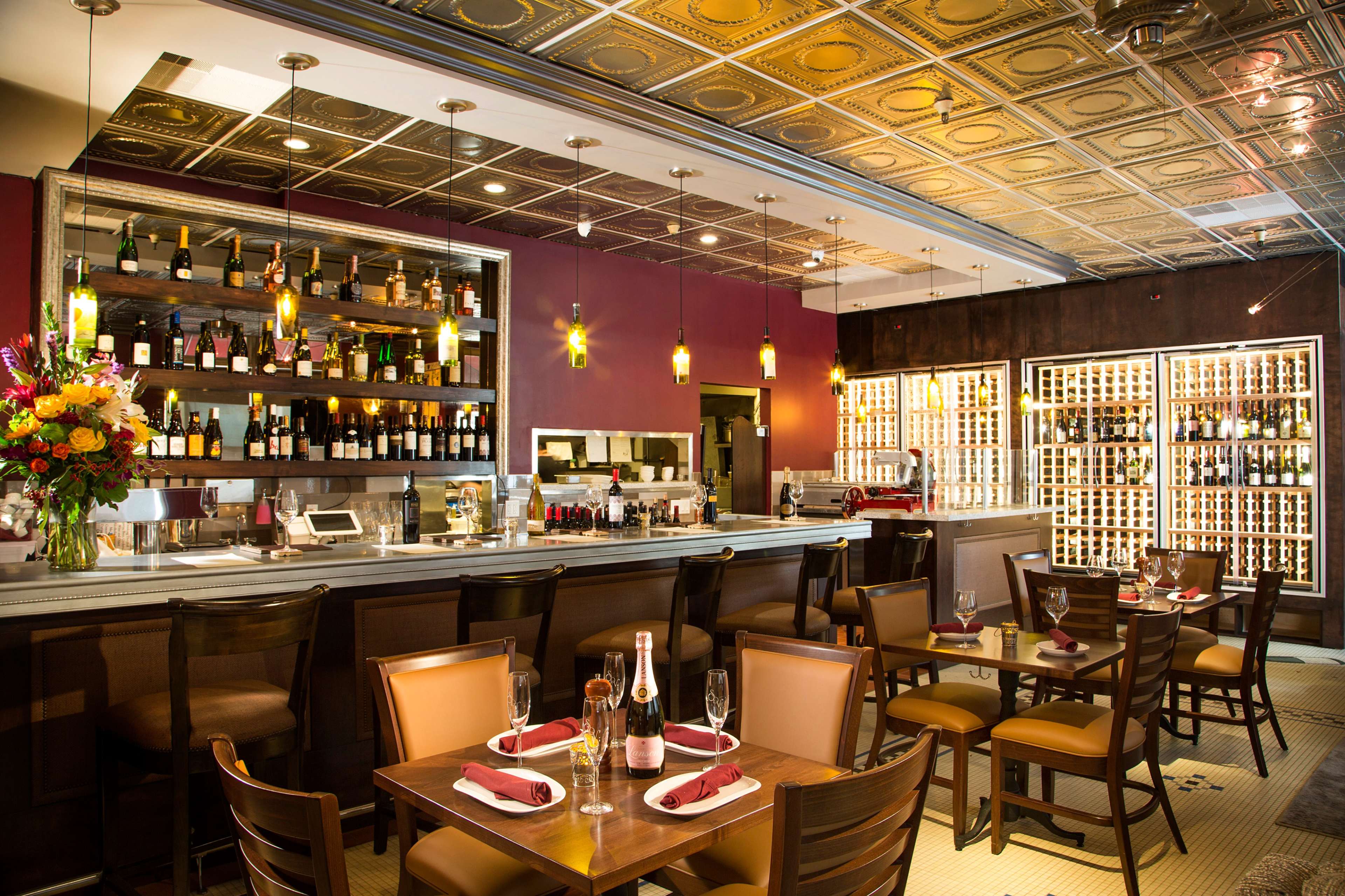 A restaurant interior featuring a stylish bar with shelves of wine and several tables set for dining.