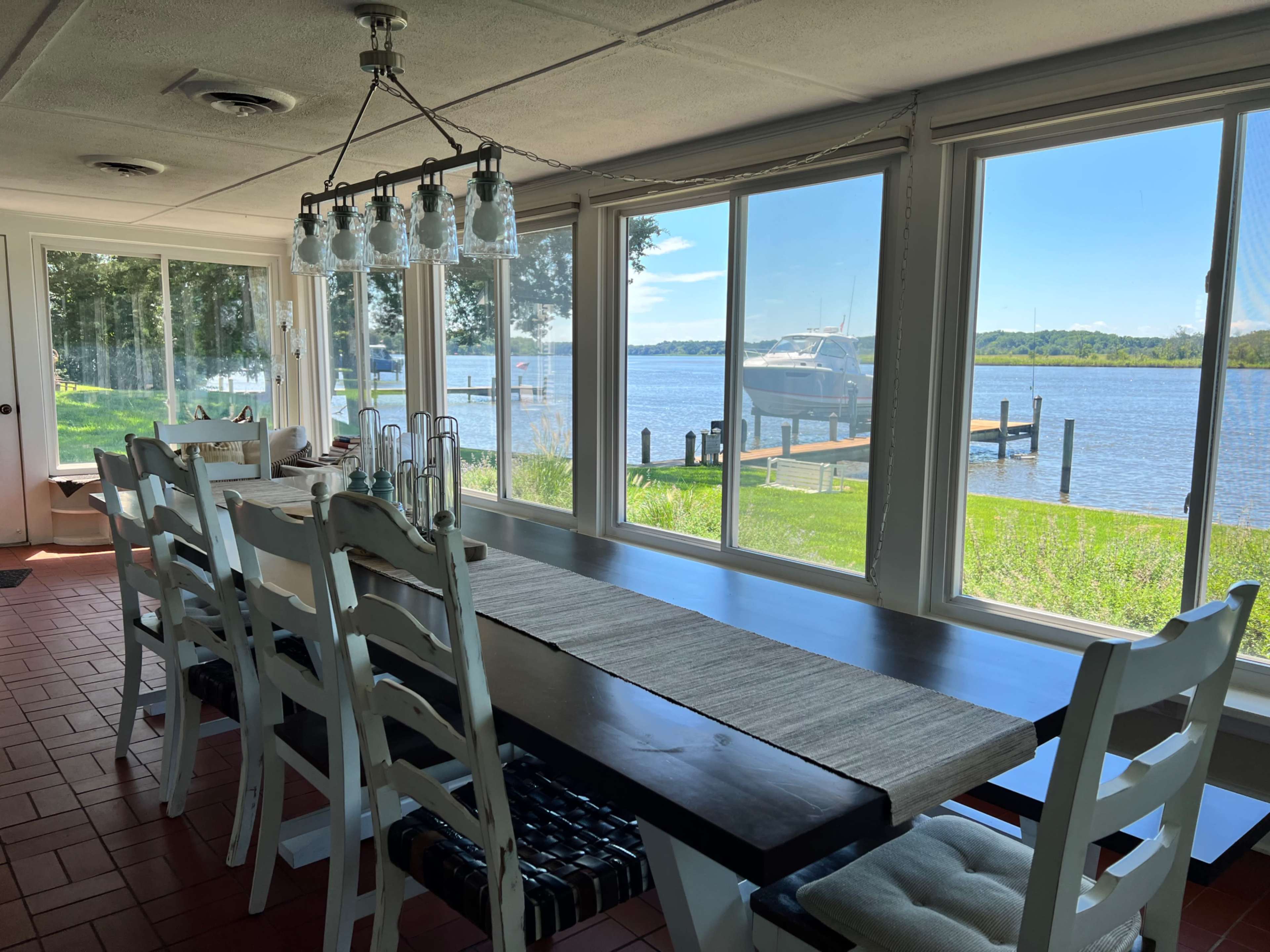 A spacious dining area with a long table overlooks a river through large windows.
