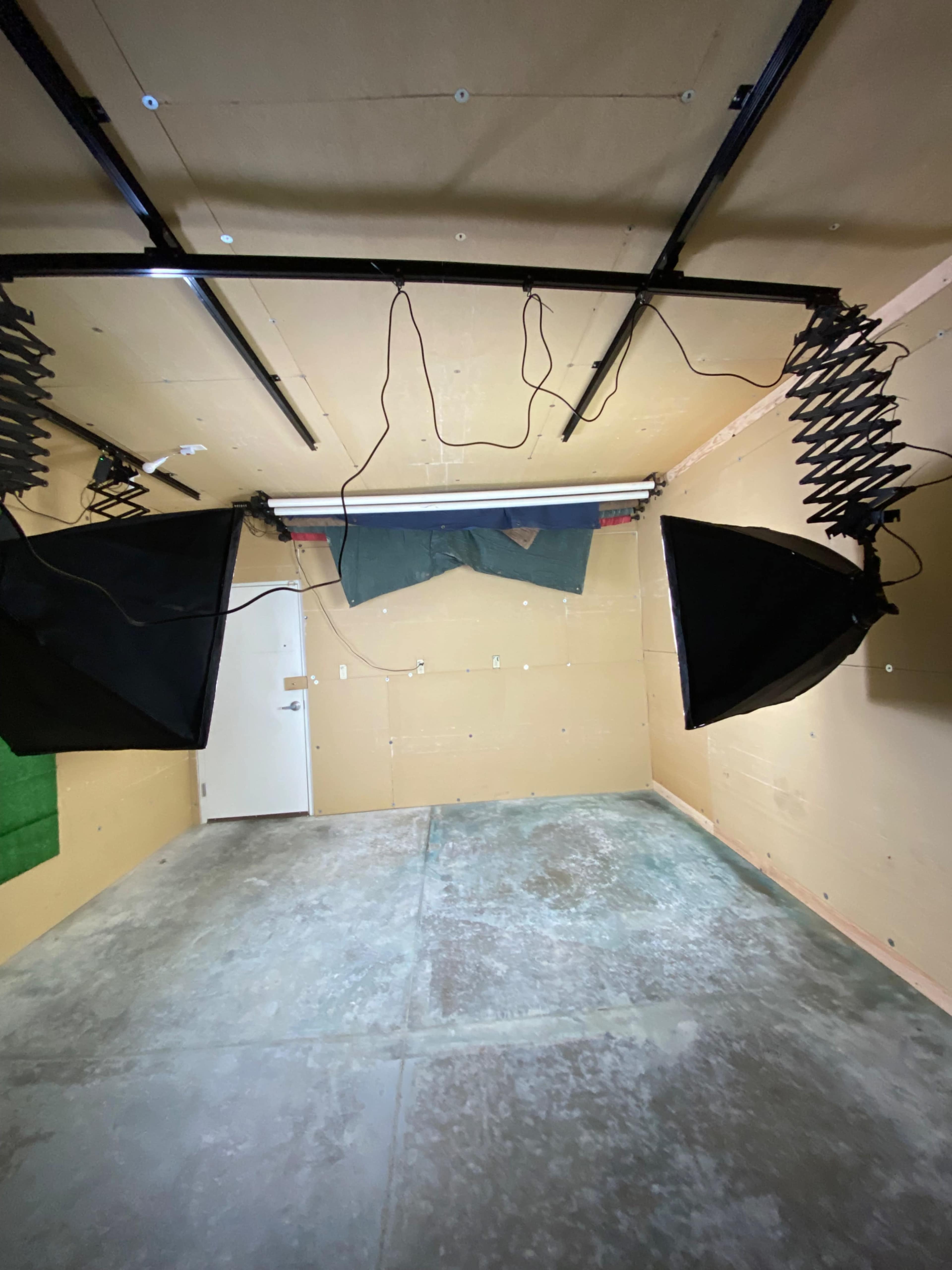 The image shows a sparsely furnished studio space with two large black backdrops suspended from the ceiling and a concrete floor.