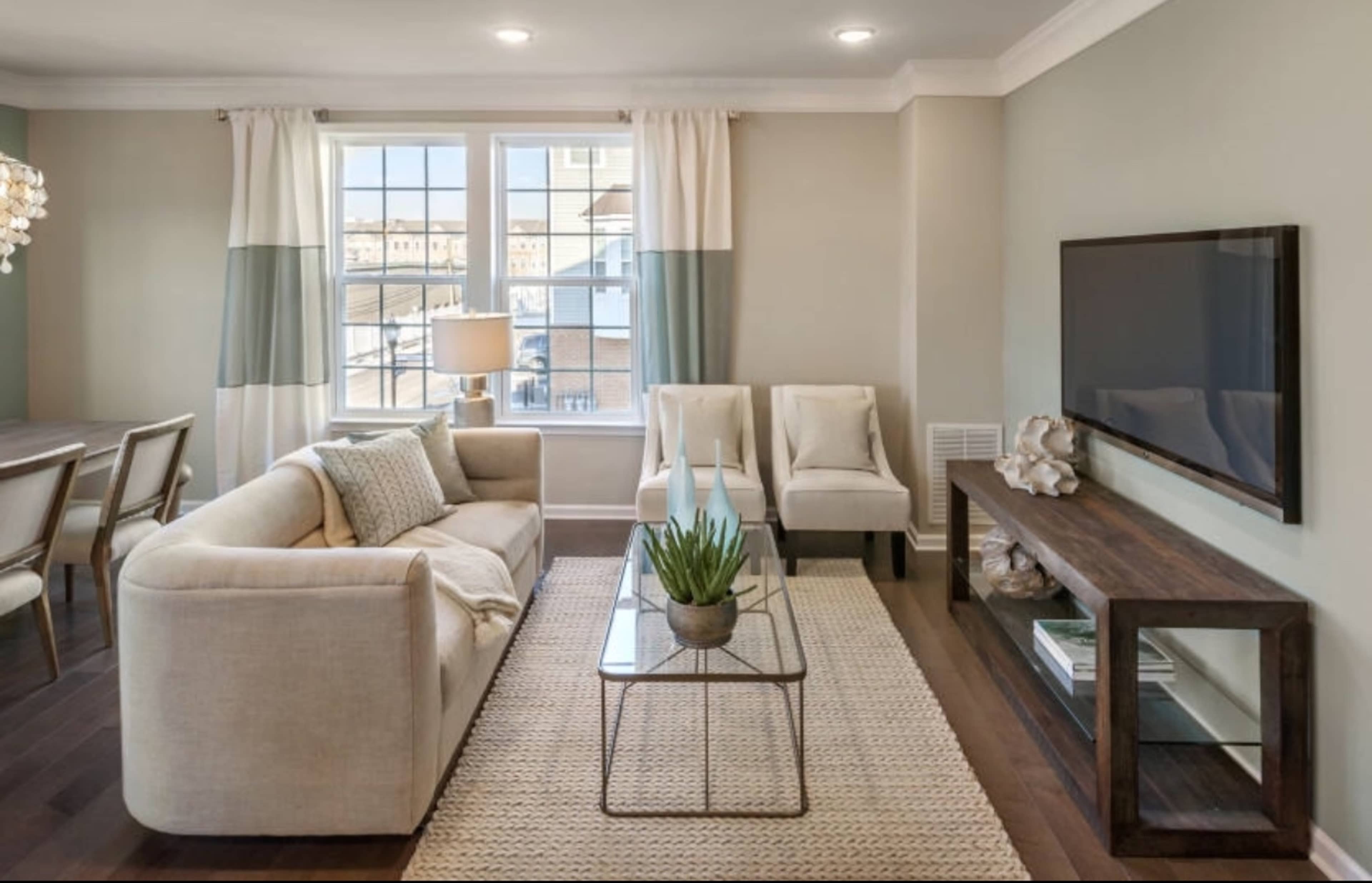 A modern living room featuring a beige sofa, two armchairs, a coffee table with a plant, and a wall-mounted television.
