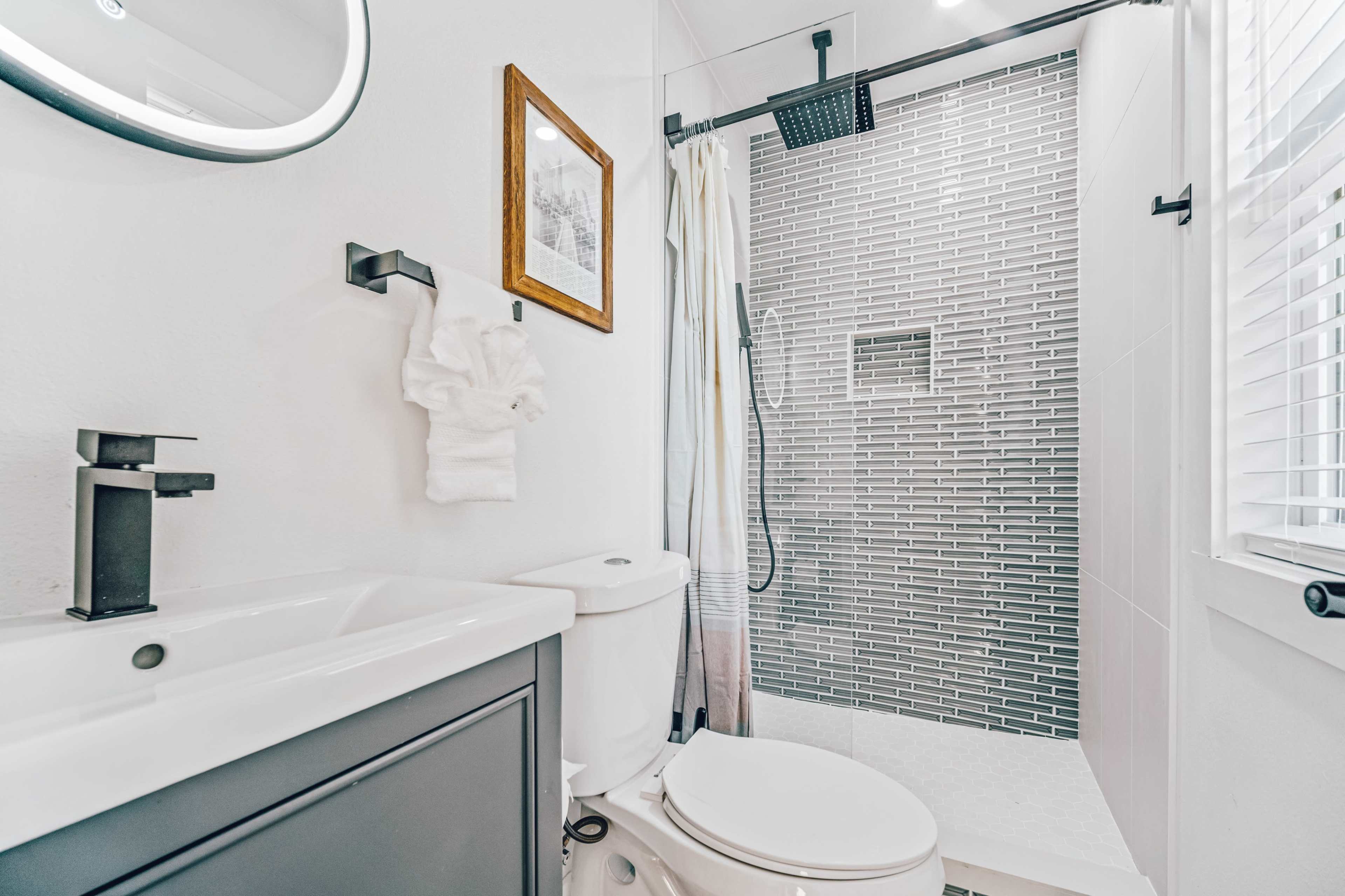 A modern bathroom with a vanity sink, a toilet, and a glass shower featuring a tiled wall.