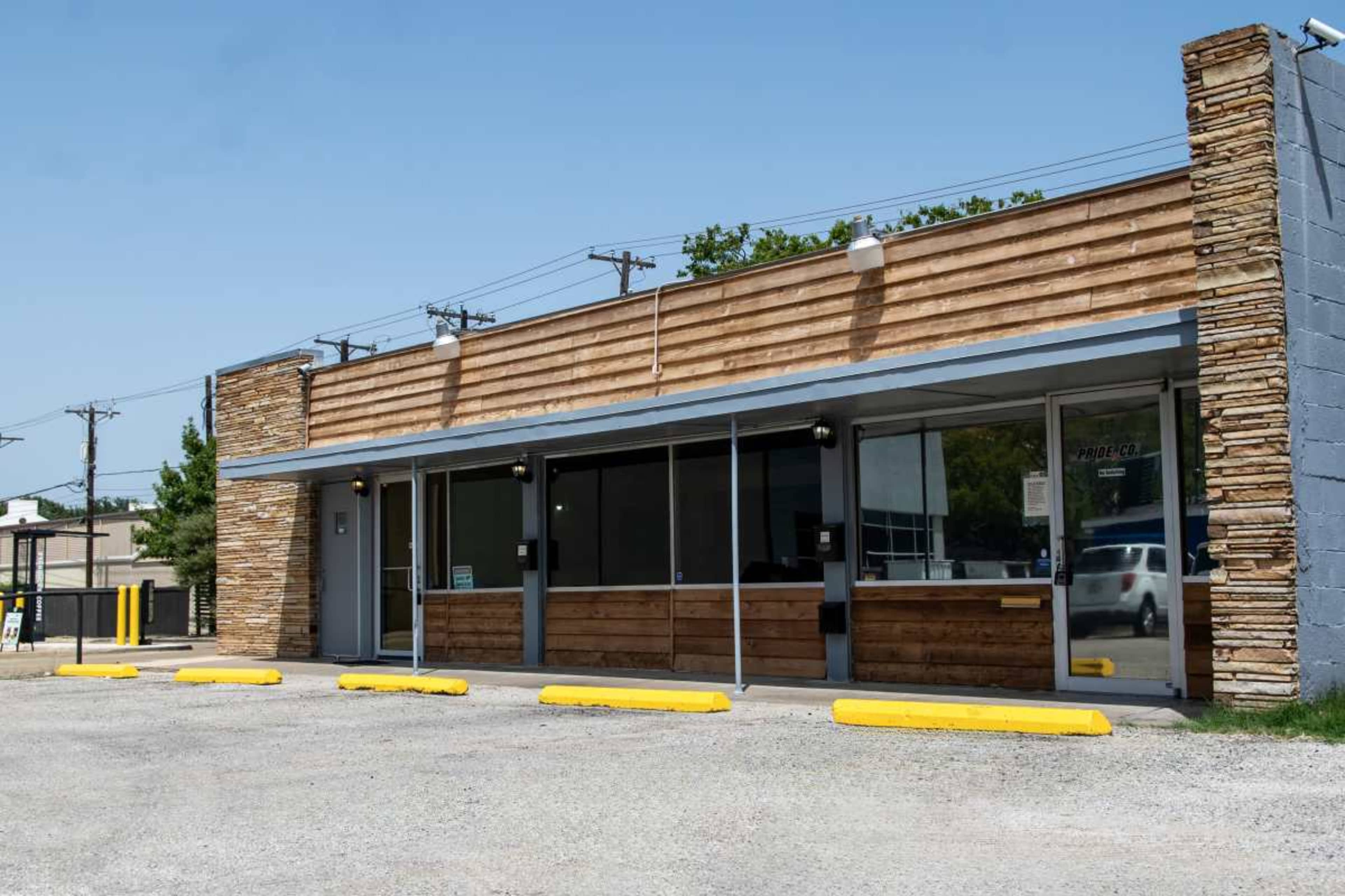 A single-story commercial building features a wooden and stone facade with large front windows and a gravel parking area.