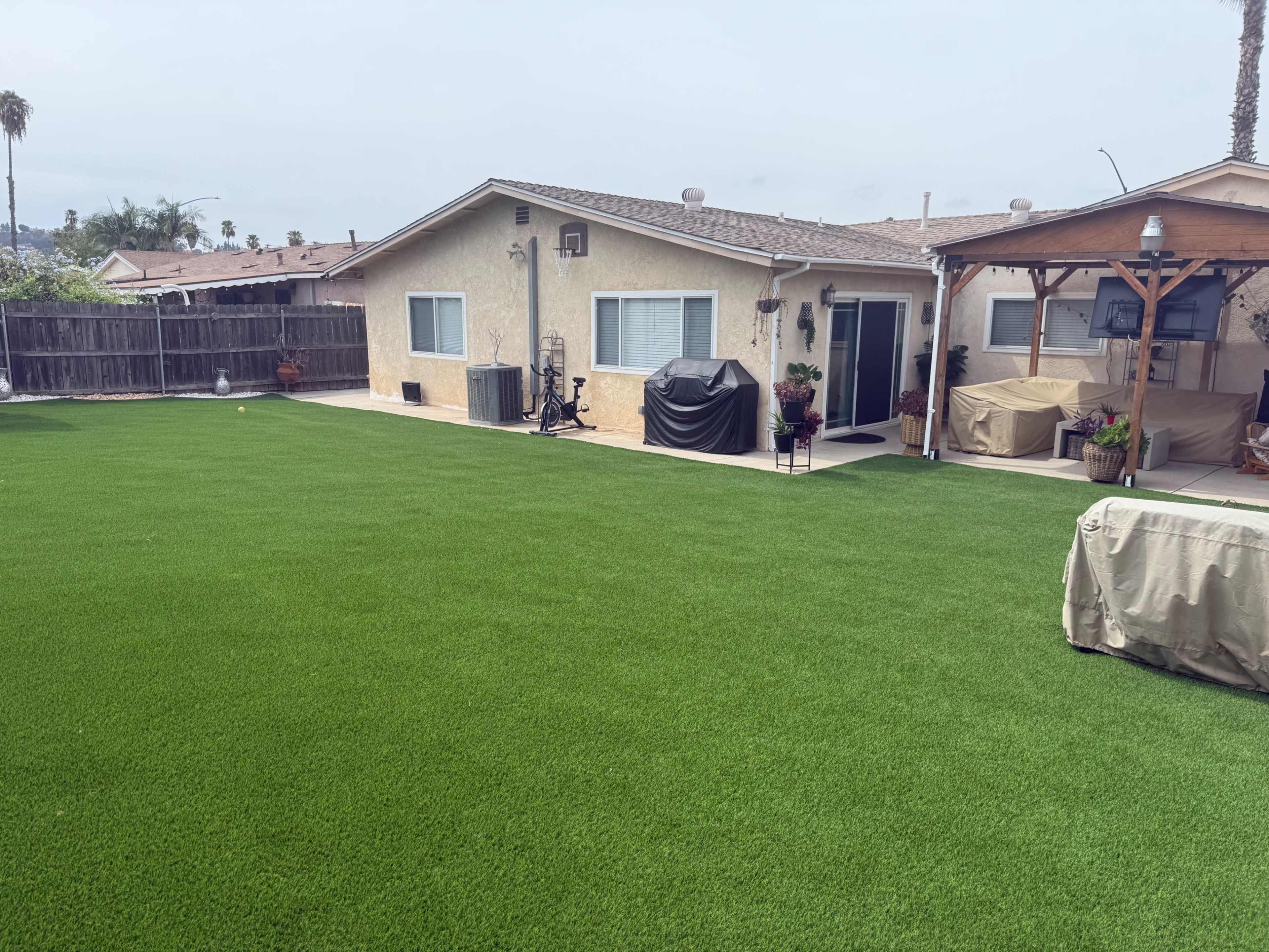The image shows a residential backyard with a green lawn, a house with a patio, and outdoor furniture.