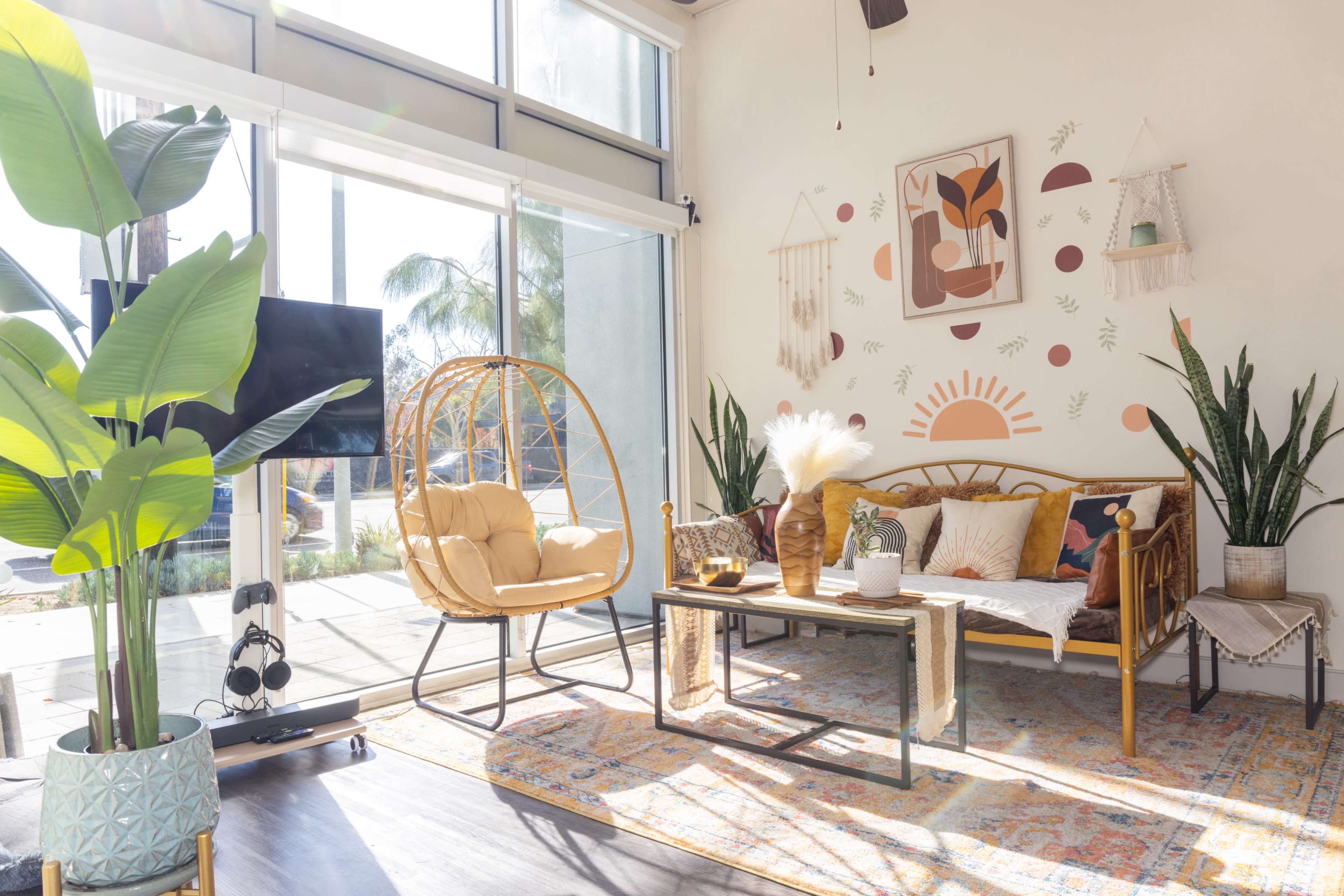 A bright, modern living room with a hanging egg chair, a sofa adorned with decorative cushions, and various indoor plants.