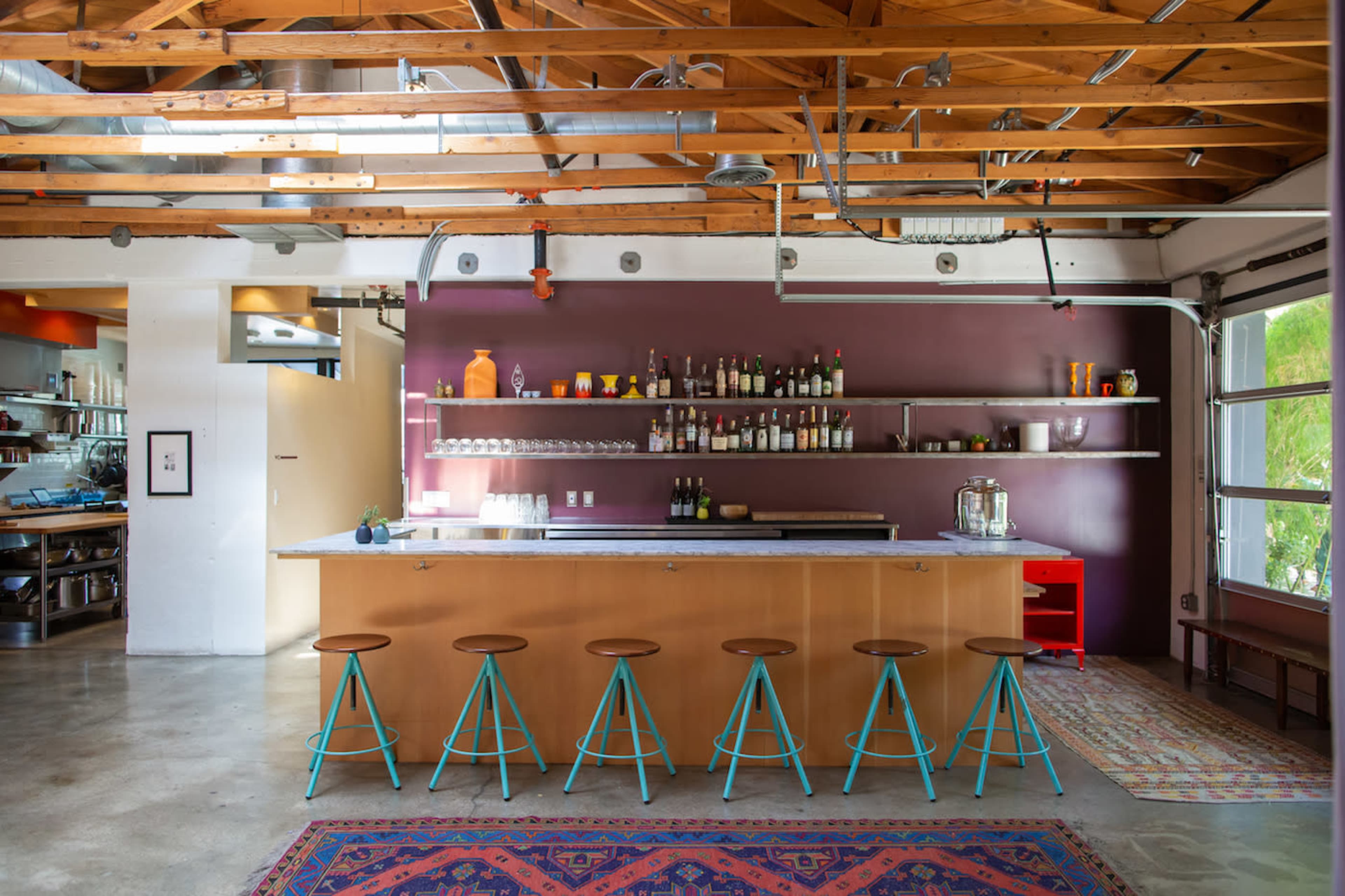 A modern kitchen with a central island bar featuring stools, open shelving displaying various bottles, and a mix of rustic and contemporary design elements.