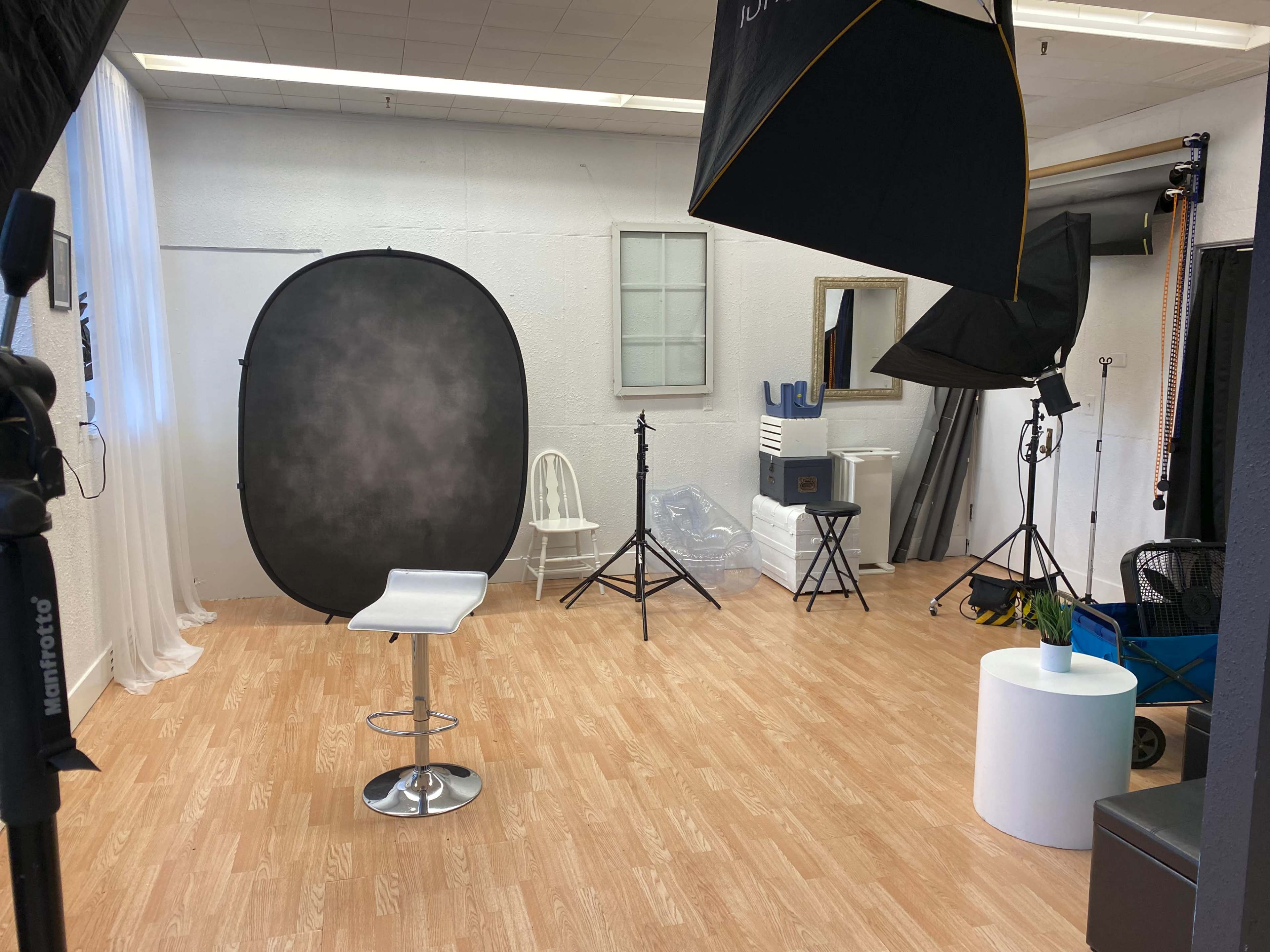 A photography studio setup with a backdrop, lighting equipment, and a stool arranged on a wooden floor.