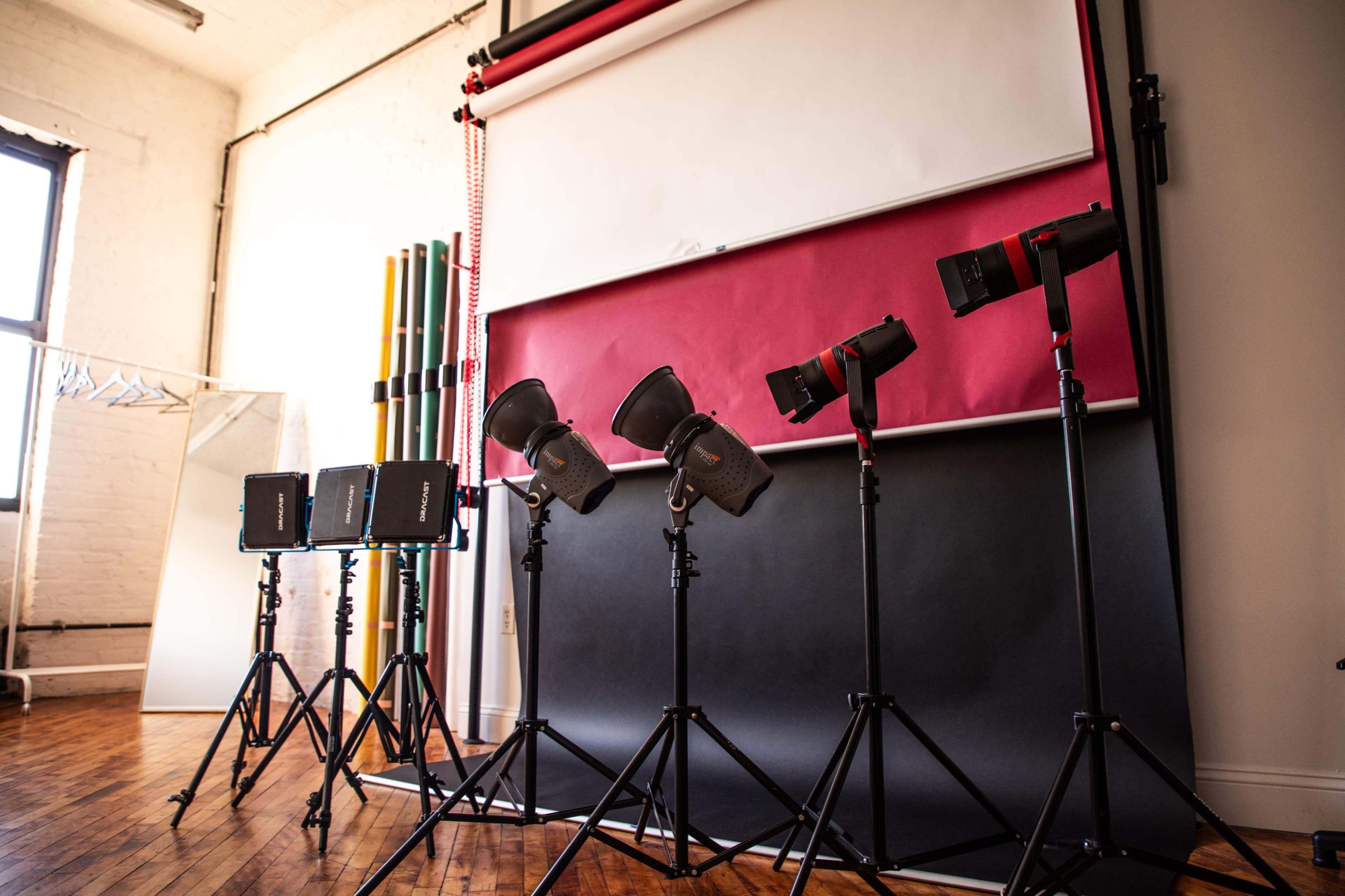 The image shows a photography studio setup with multiple lights on tripods and a variety of colored backdrops.