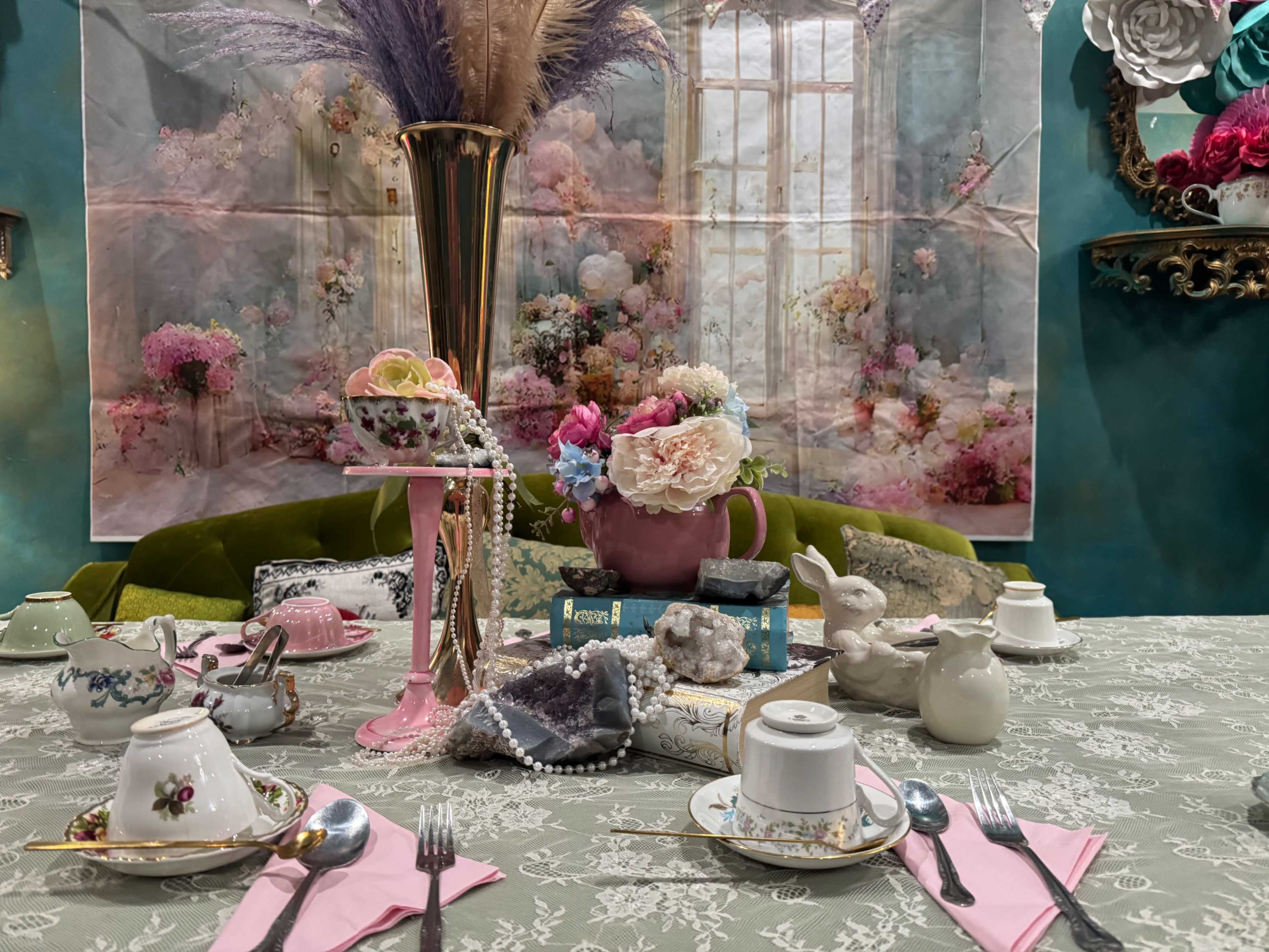The image depicts a decorative table set for tea with an array of vintage china, flowers, and a pastel backdrop featuring a floral scene.
