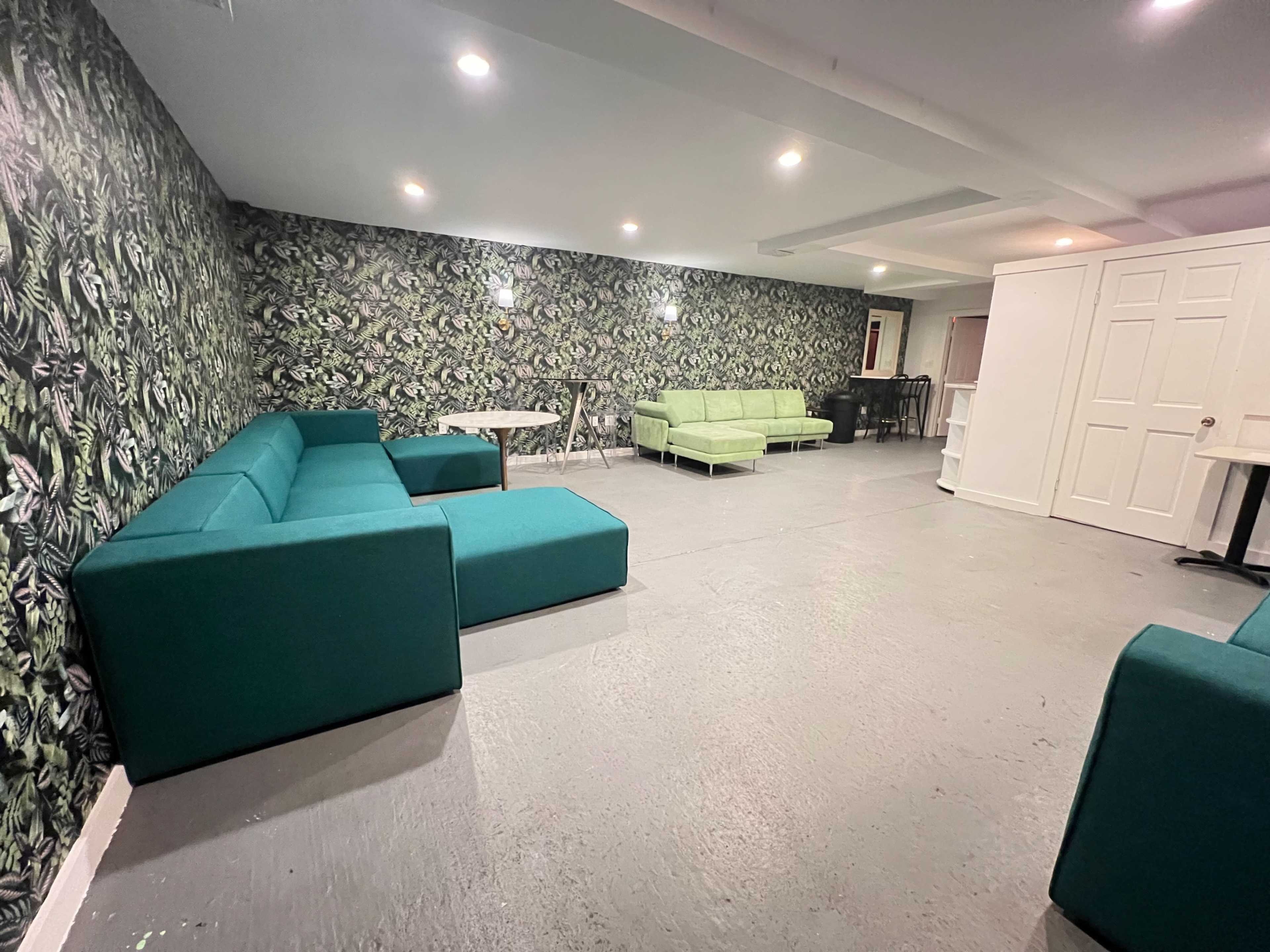 A spacious room with green sofas, a round table, and a patterned wall featuring a floral design.