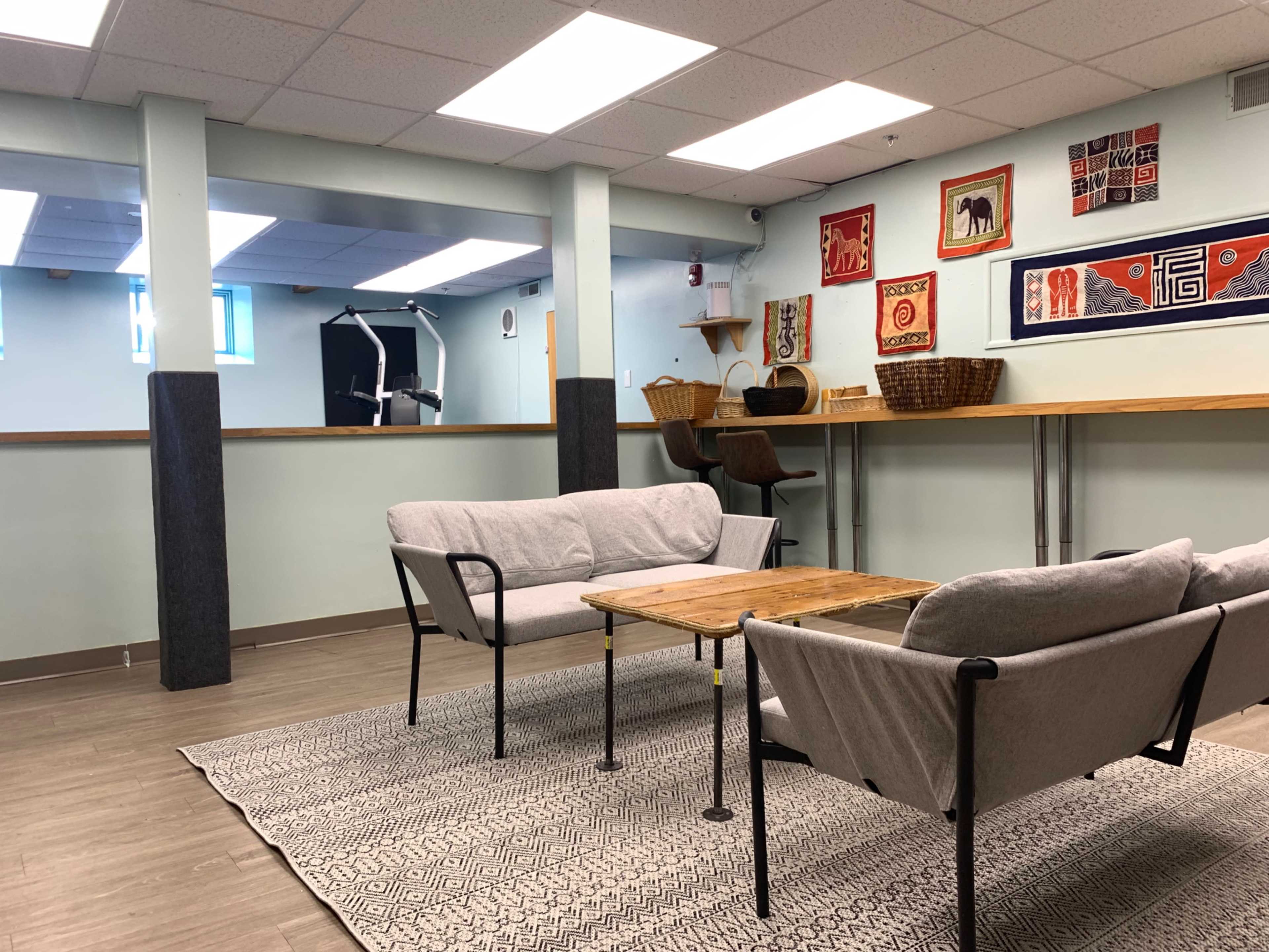 The image shows a casual lounge area with two couches, a wooden coffee table, and decorative wall hangings.