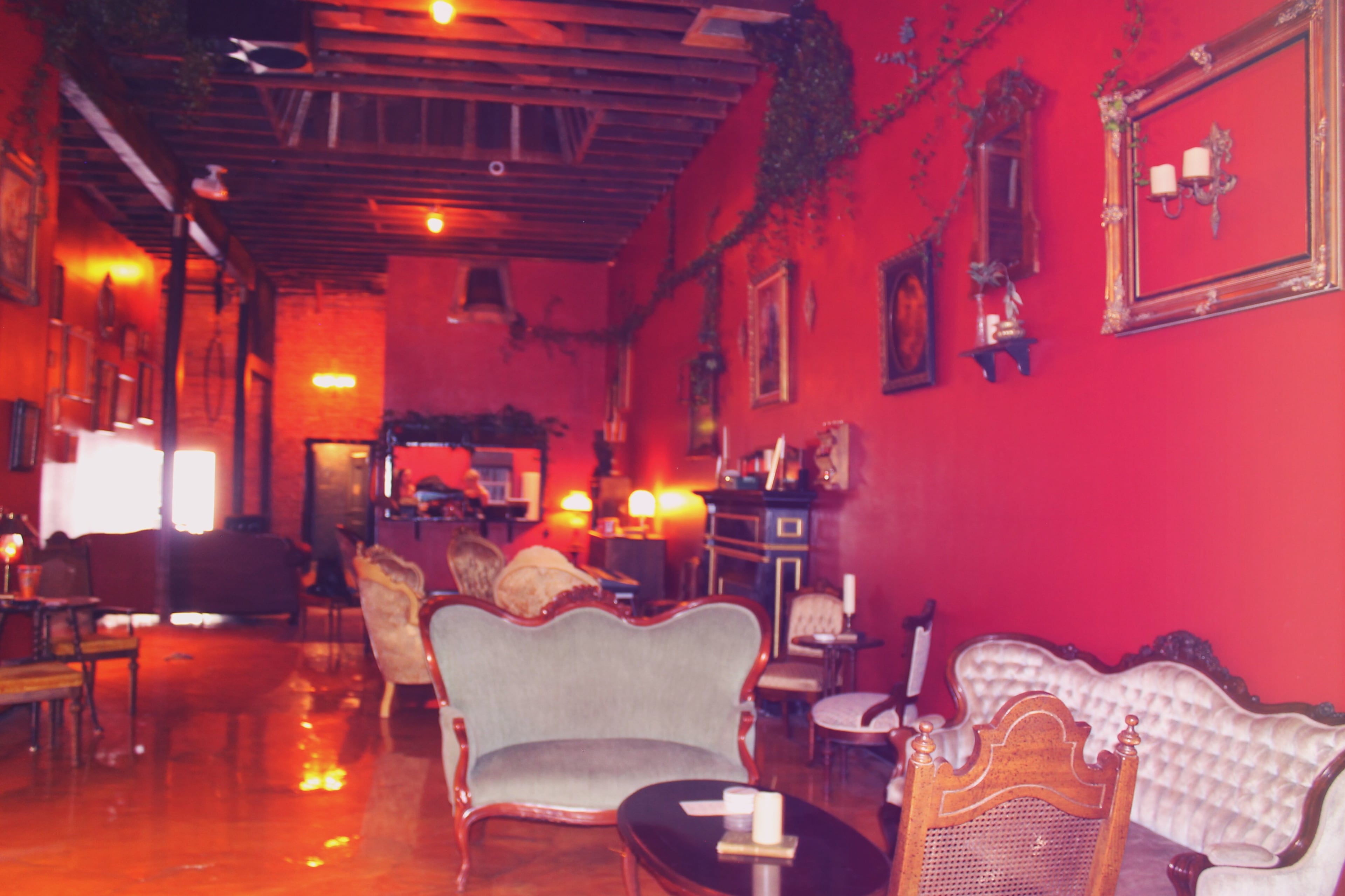 The image shows a cozy lounge with red walls, vintage furniture, and decorative elements, creating an inviting atmosphere.