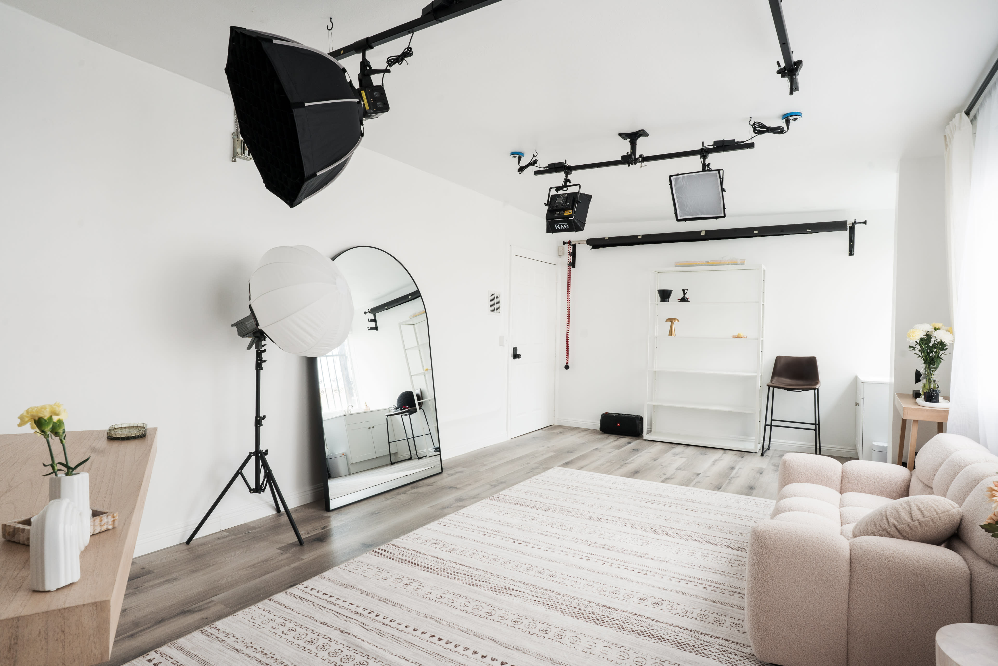 The image shows a well-lit, modern studio space featuring a large mirror, a soft sofa, and a minimalistic shelf against a wall.