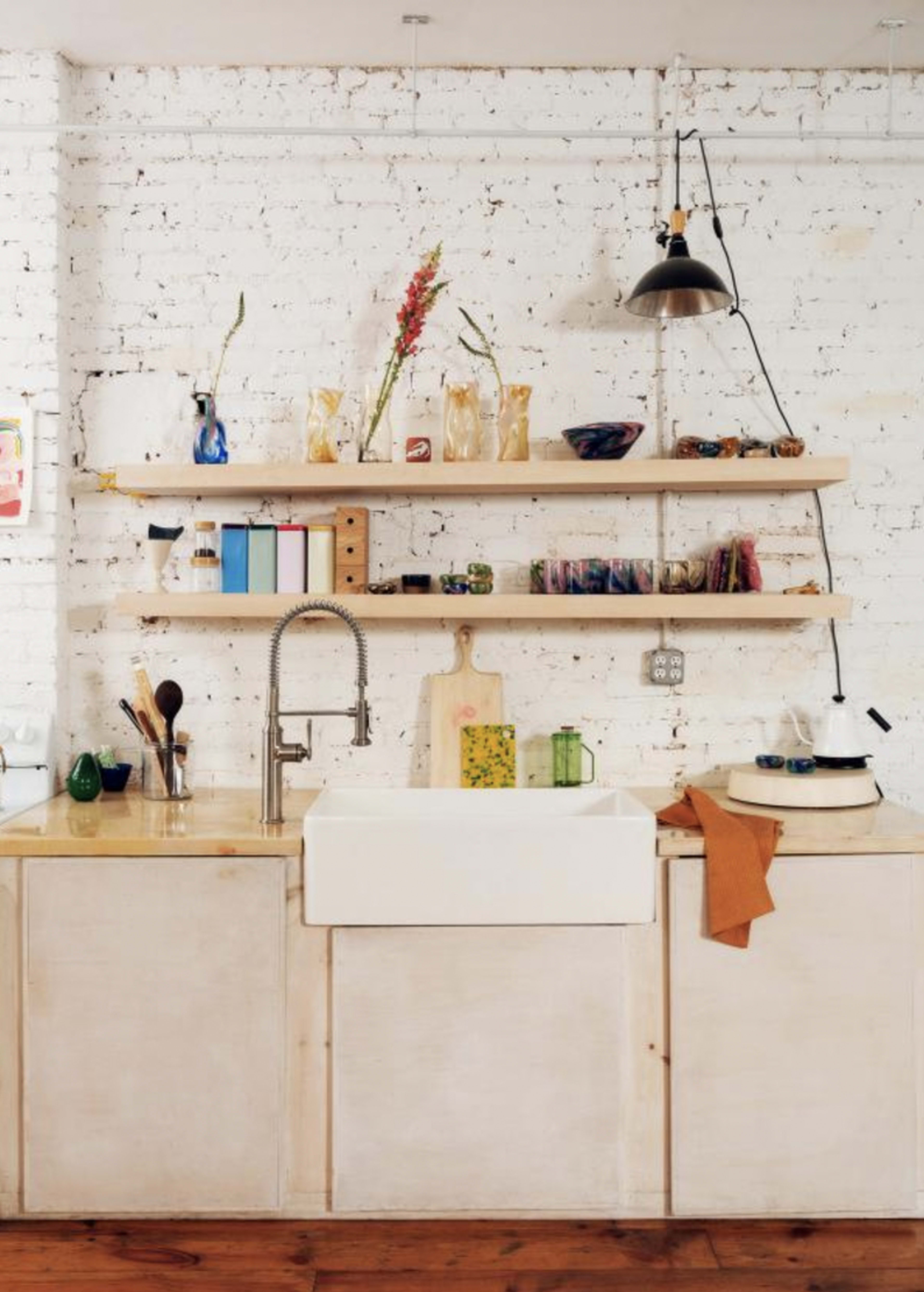 The image shows a white-brick wall with a sink and wooden shelves displaying various kitchen items.