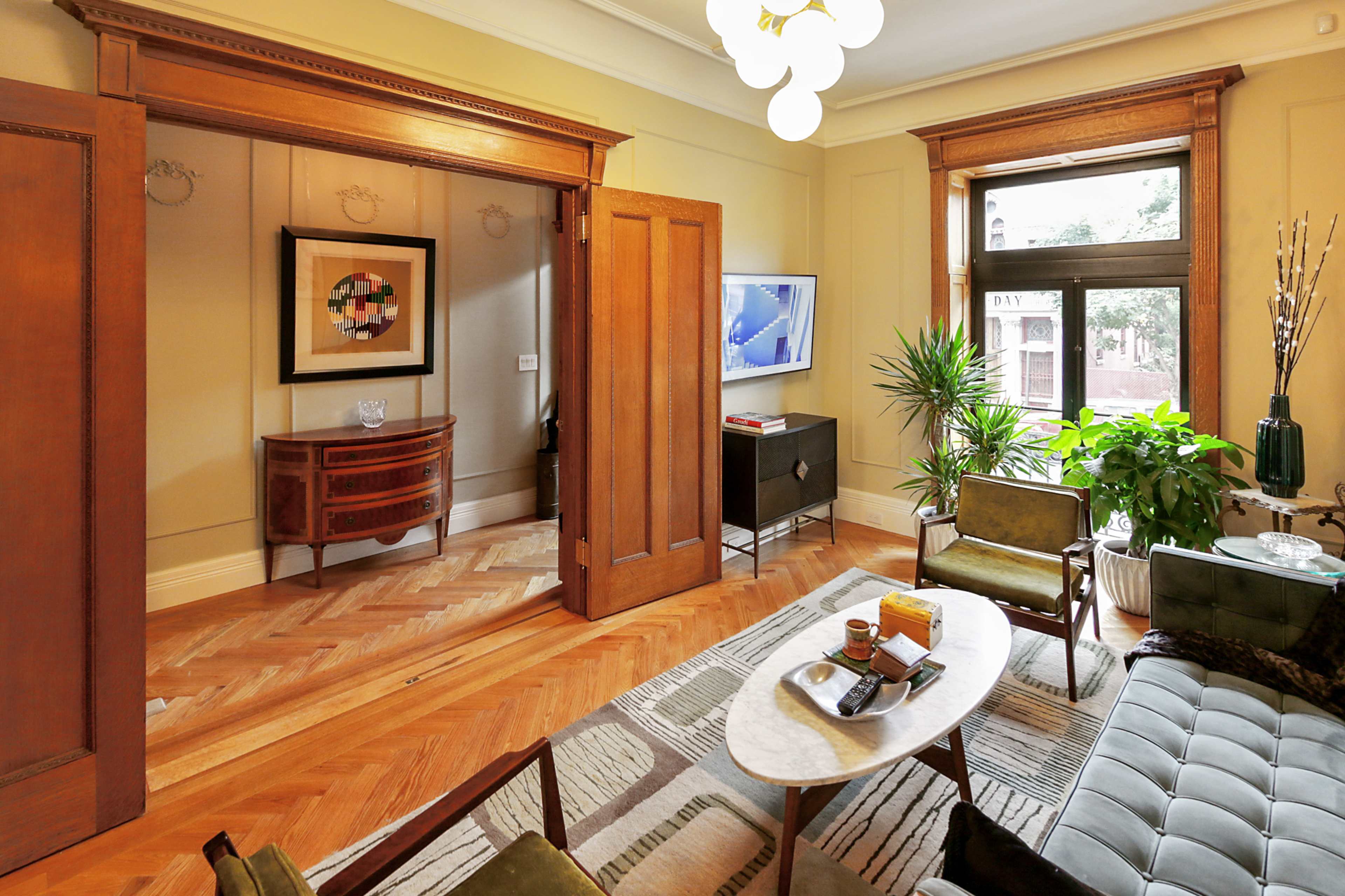 A well-furnished living room featuring a green sofa, a marble coffee table, and wooden doors leading to another room.