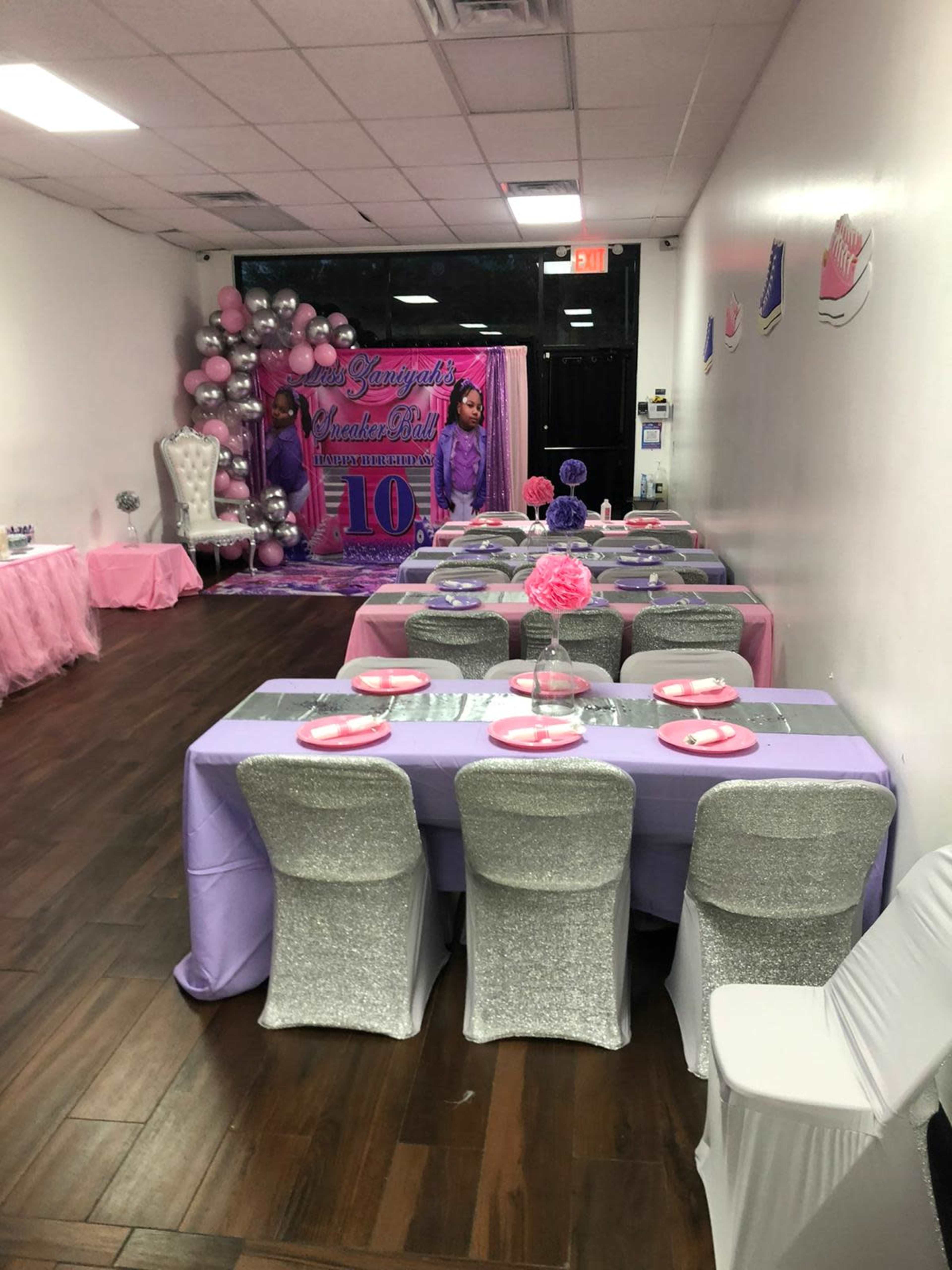 A decorated party venue with tables set in purple and silver, featuring a backdrop for a 10th birthday celebration.