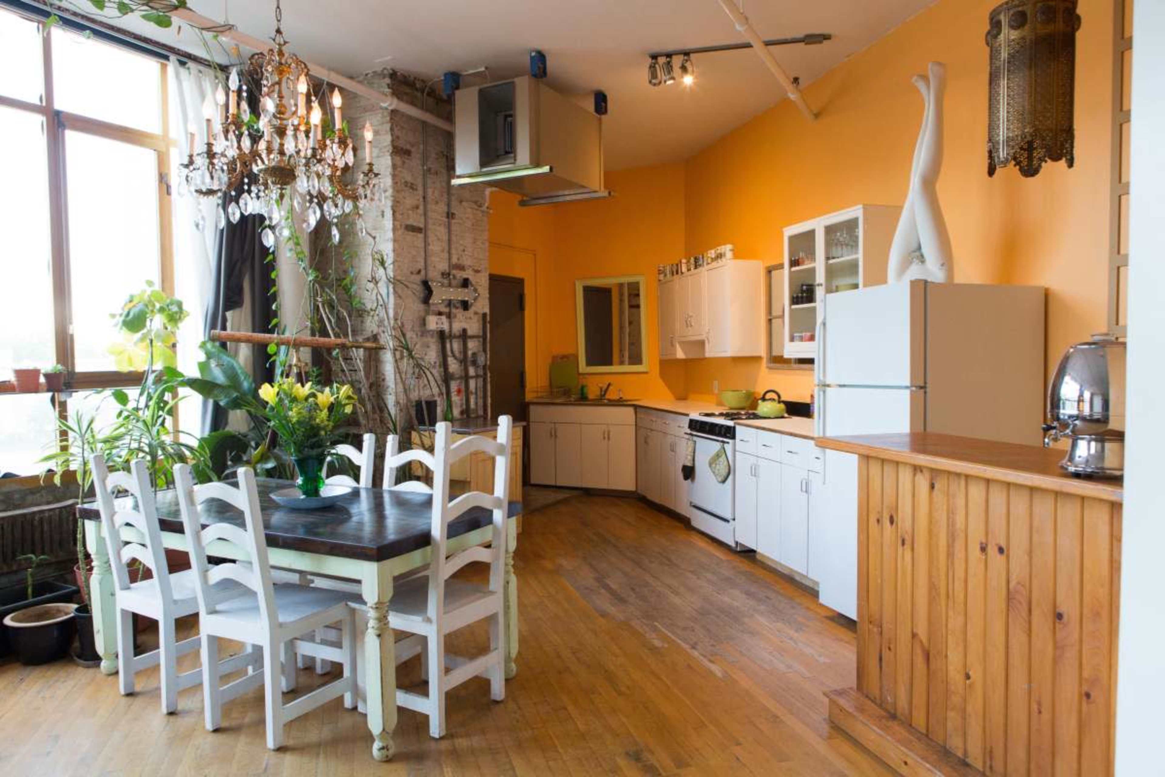 A spacious kitchen with white cabinets, a wooden dining table surrounded by chairs, and large windows allowing natural light to enter.