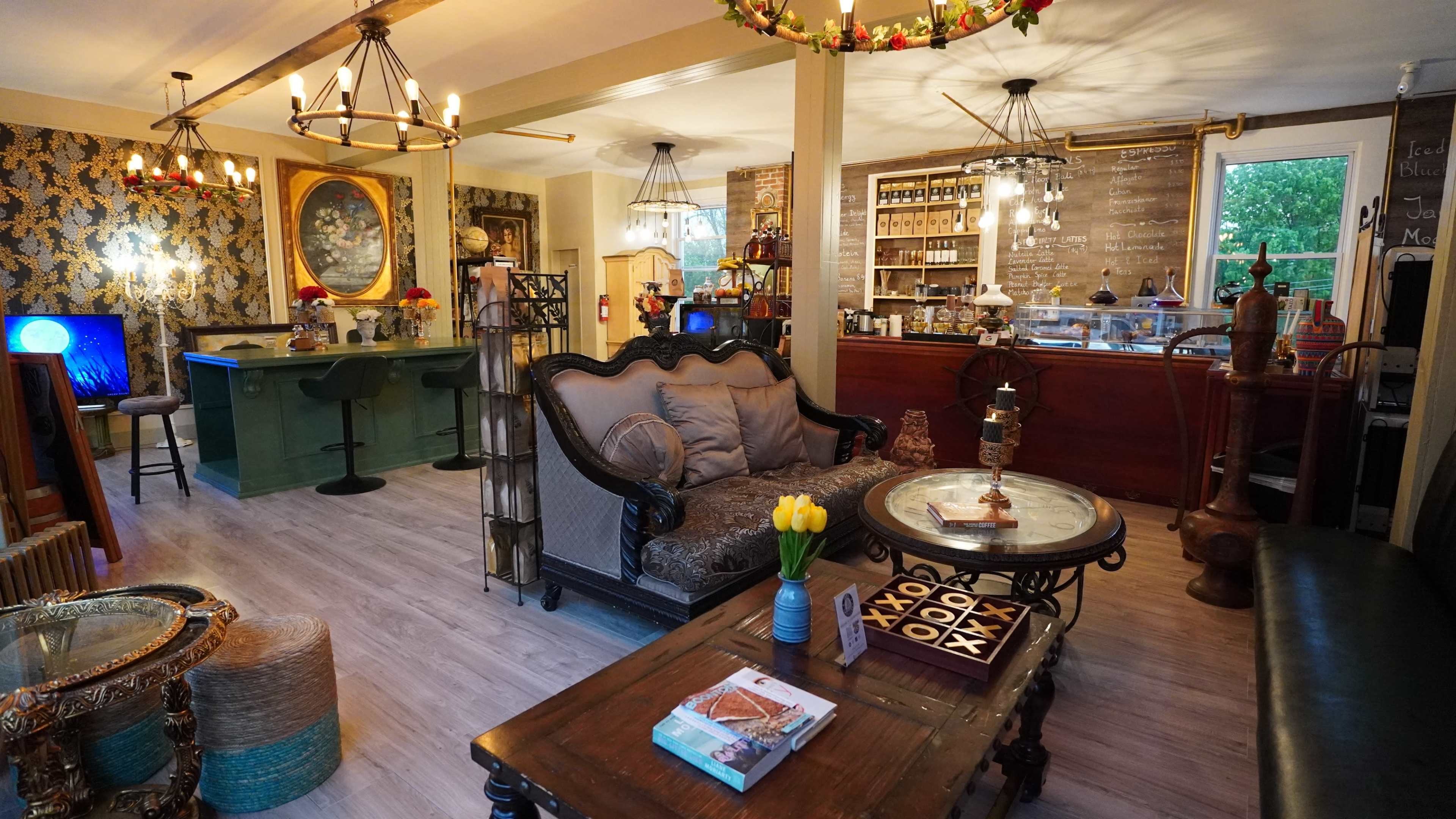 A cozy café interior featuring vintage furniture, a wooden counter, decorative lighting, and floral accents.