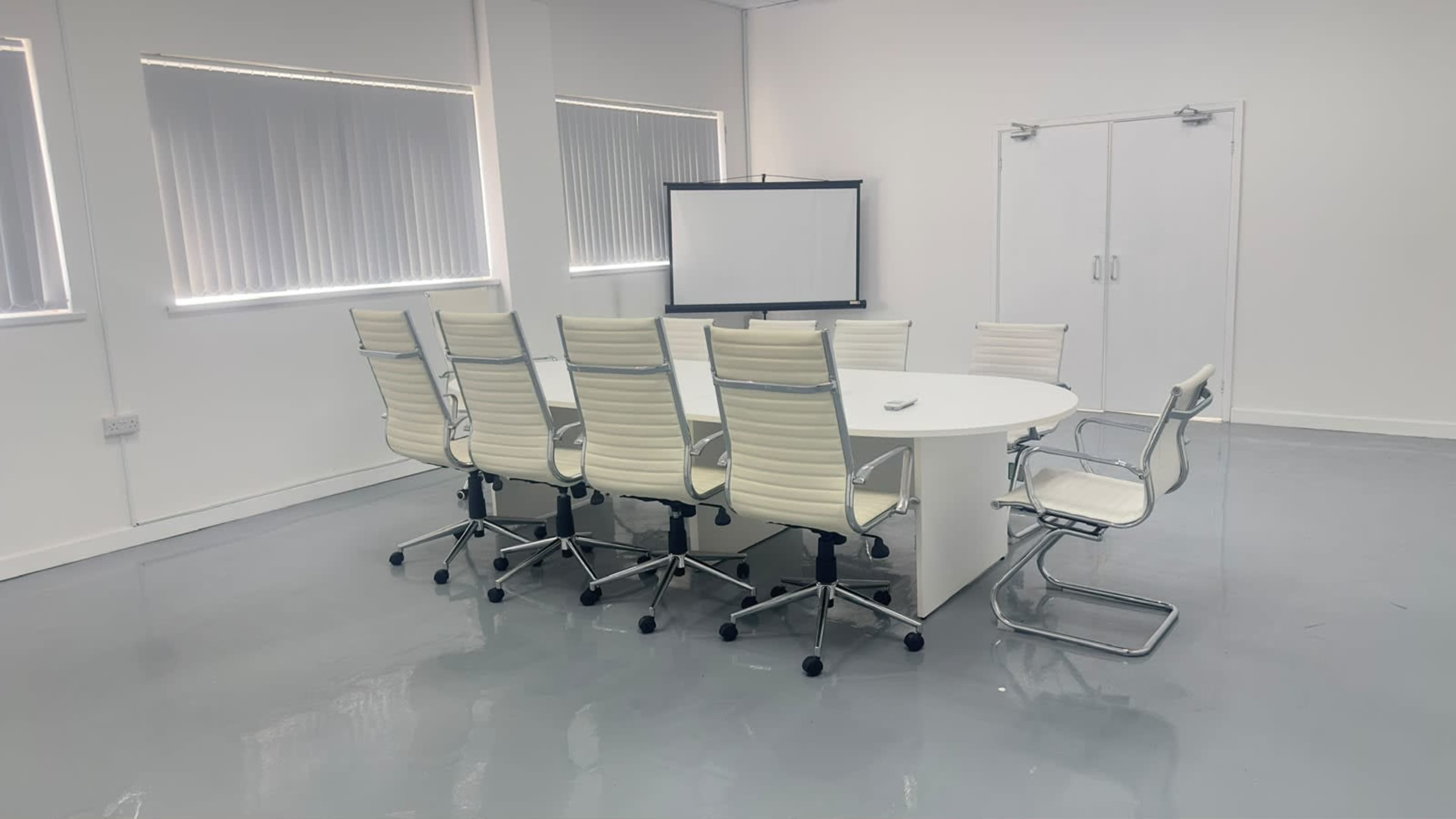 A modern conference room features a round table surrounded by high-back chairs, with a whiteboard in the background and large windows providing natural light.