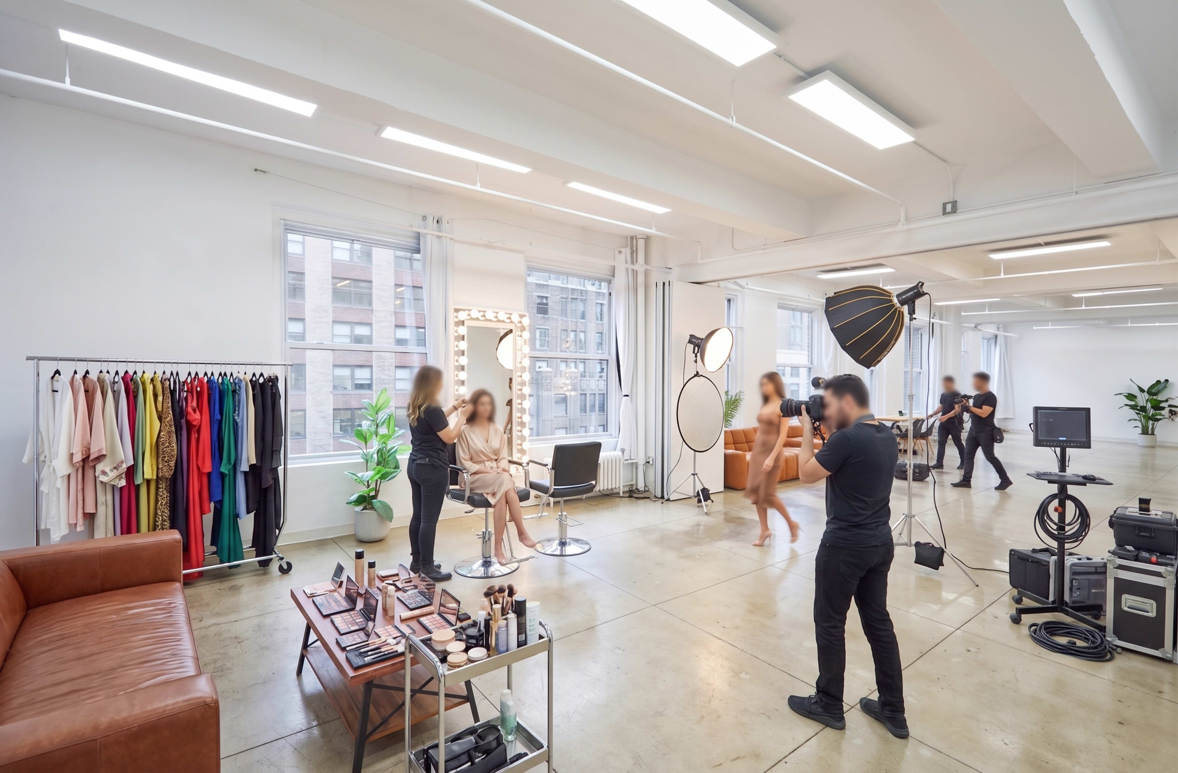 A spacious studio features a makeup station, clothing rack, and several individuals engaged in a photoshoot.