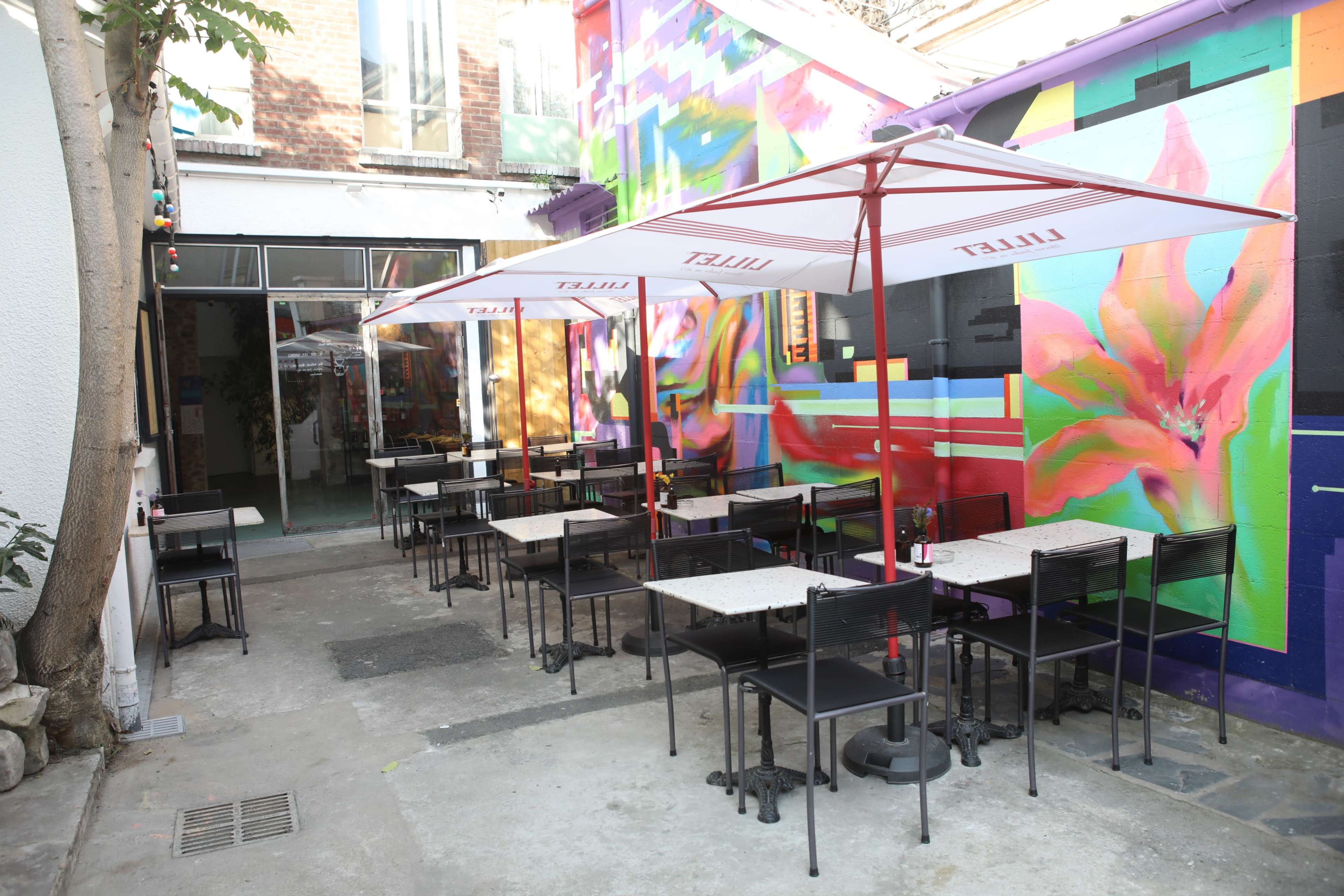 A vibrant outdoor seating area features tables and umbrellas in front of a colorful wall mural.