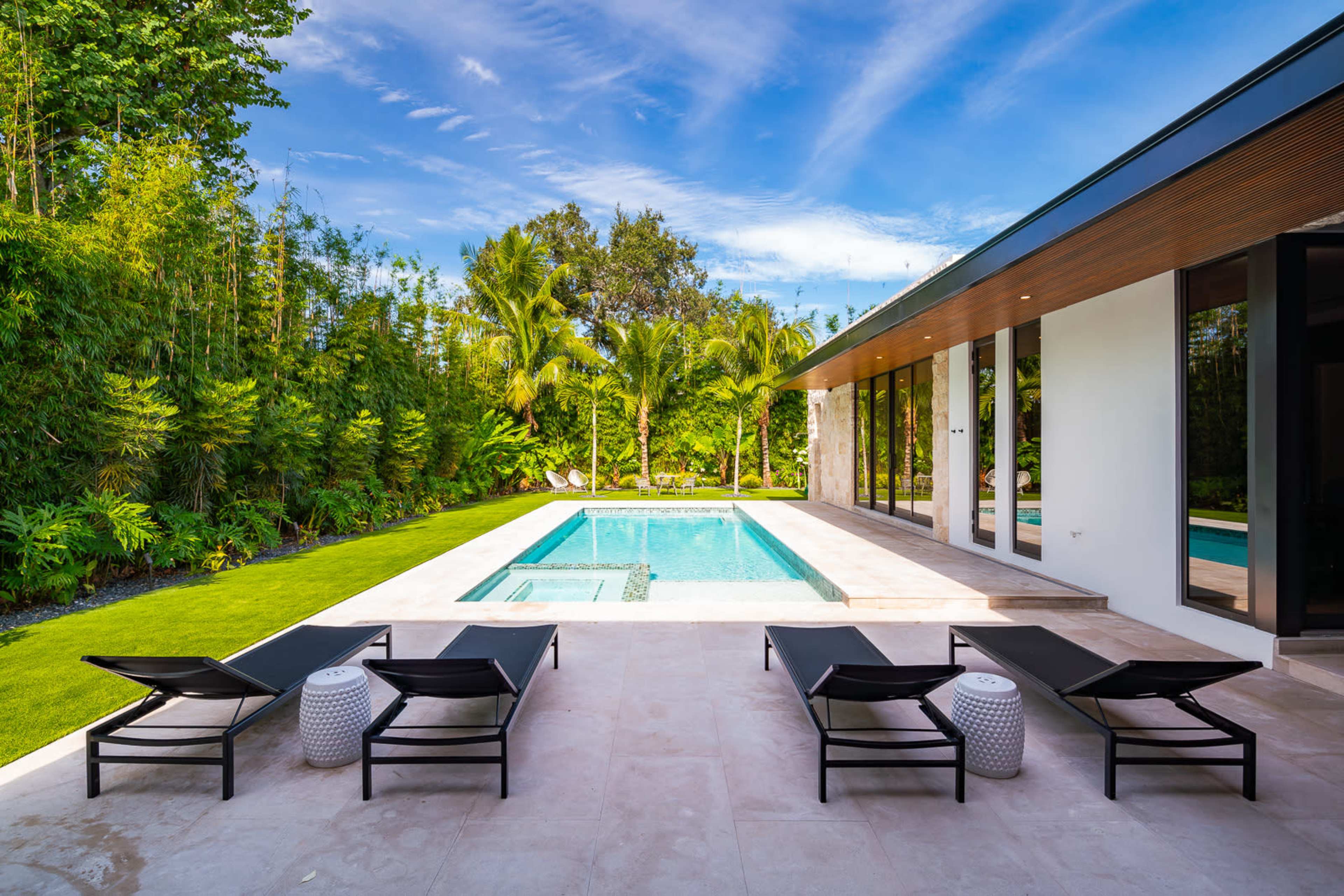A modern house features a swimming pool surrounded by lounge chairs and lush greenery.