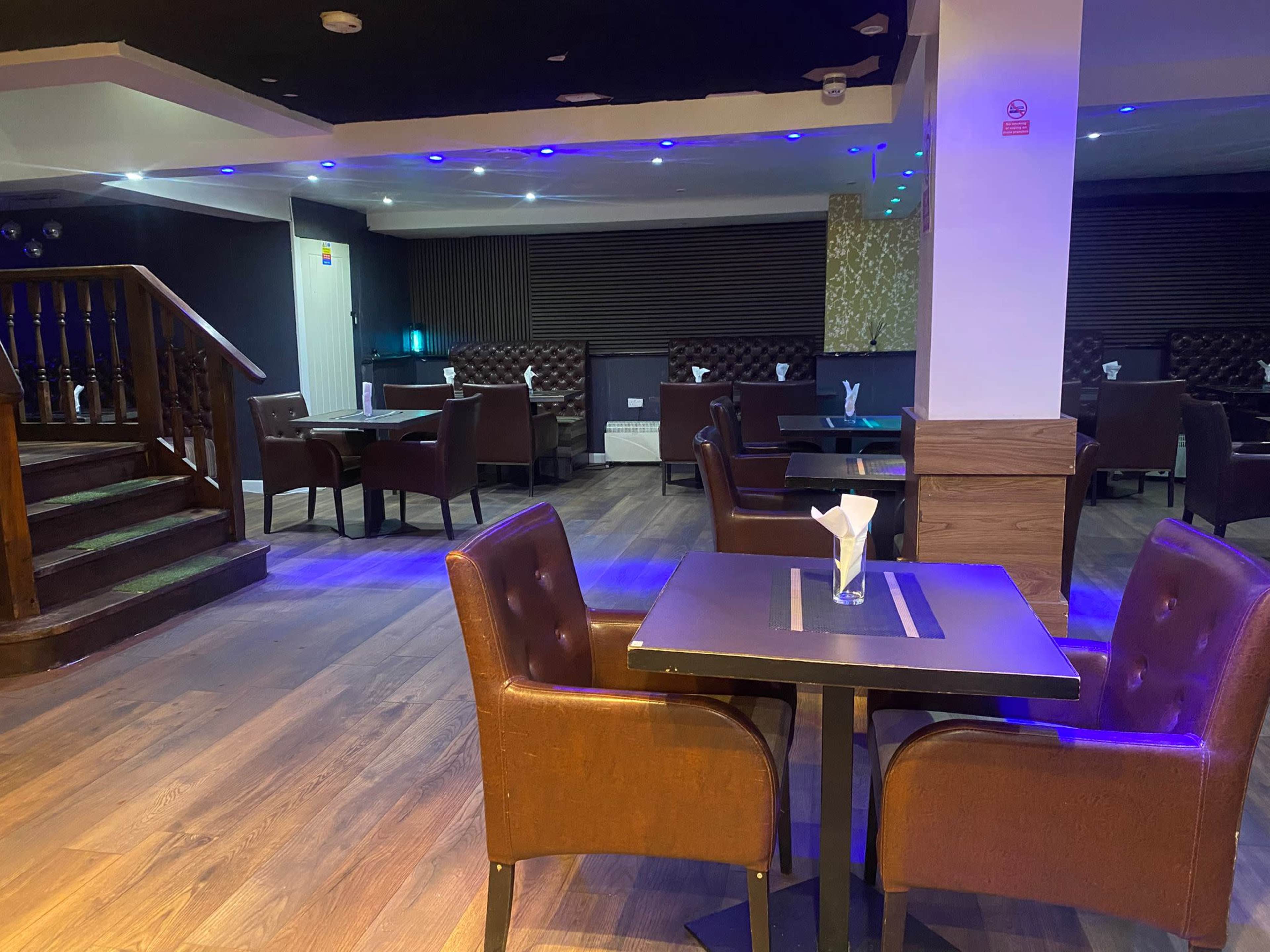 The image shows a modern restaurant interior featuring brown leather chairs and tables arranged in an open space with dim lighting and wooden flooring.