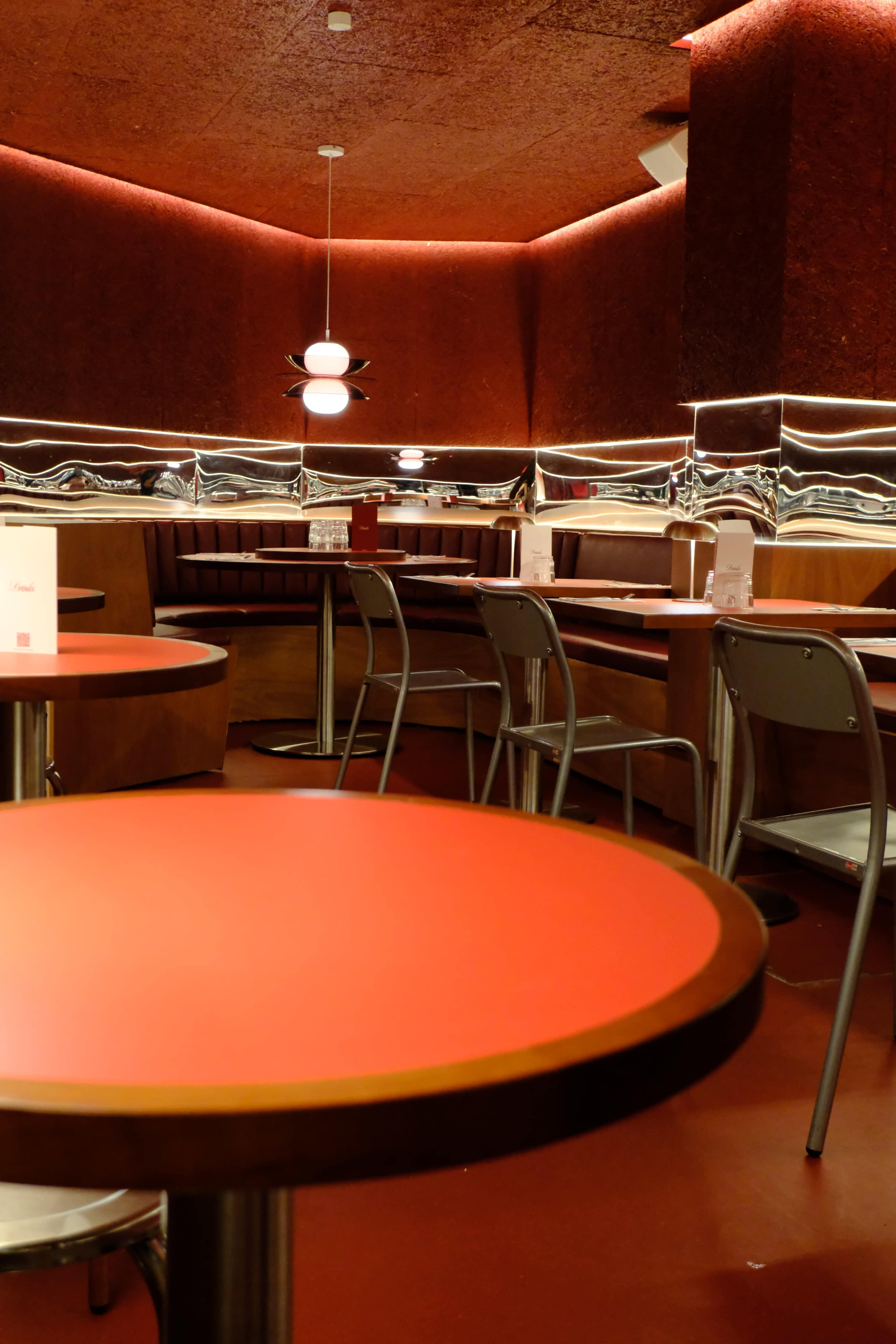 The image shows a modern diner interior with red walls, rounded seating booths, and circular tables.
