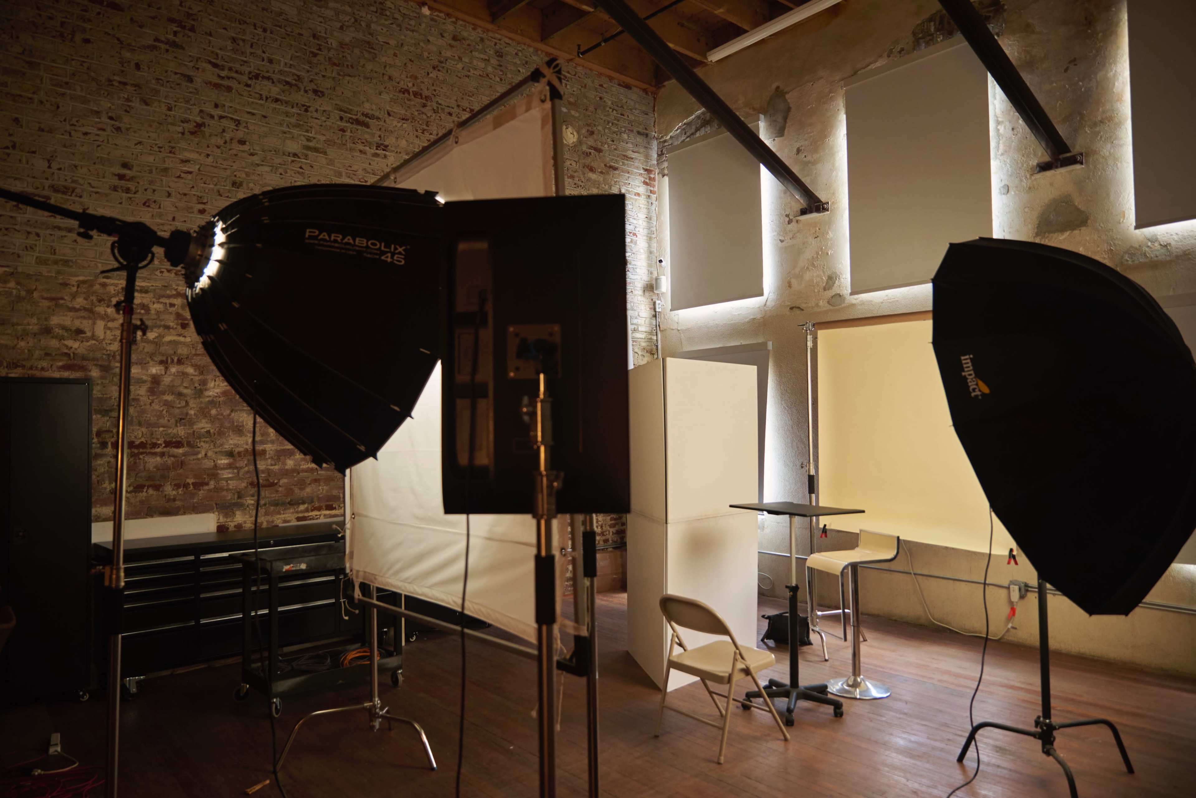 A photography studio is set up with softboxes, lighting equipment, and a backdrop against a brick wall.