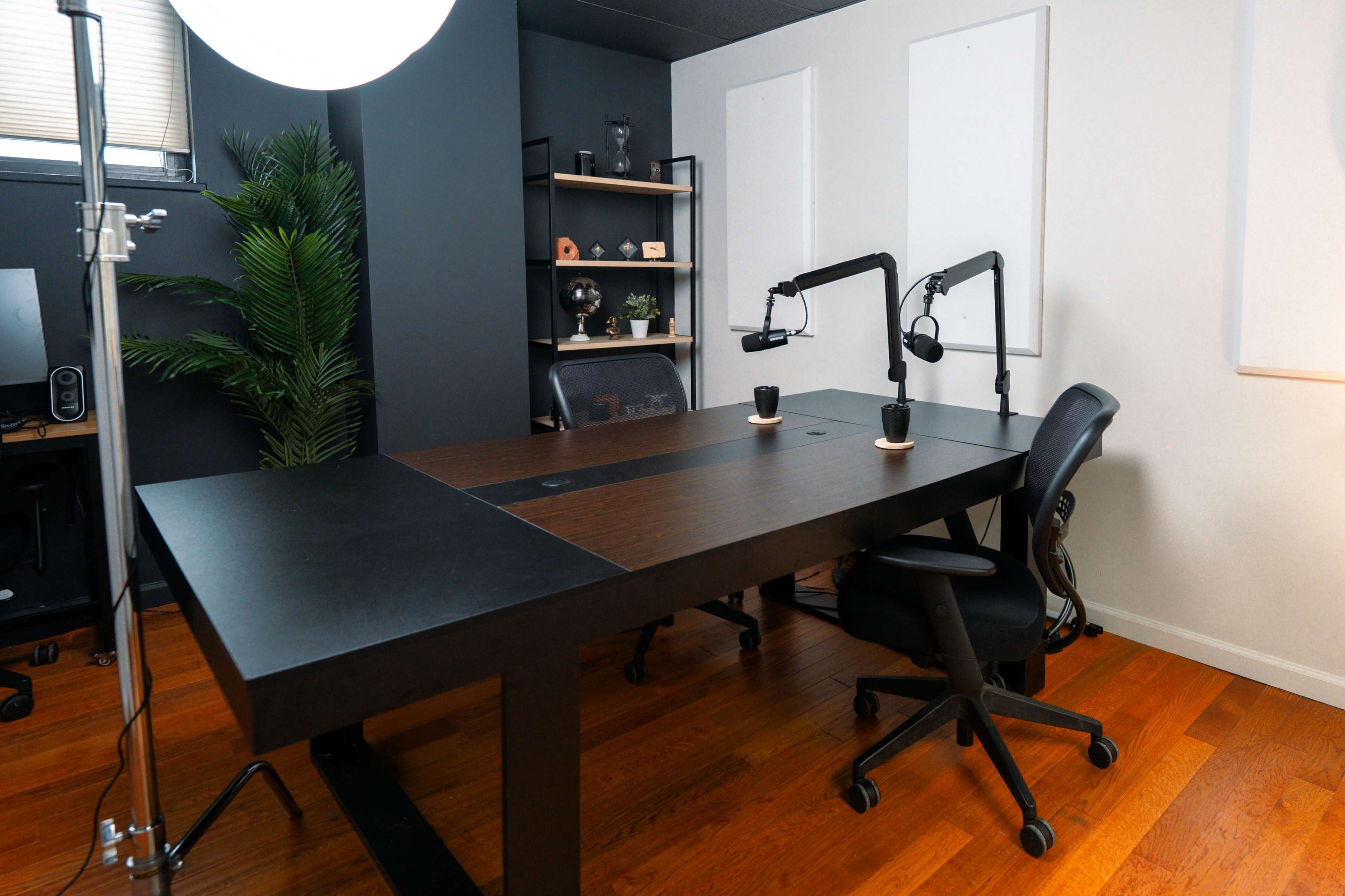 The image shows a modern office space with a large black desk, two chairs, and soundproofing panels on the wall.