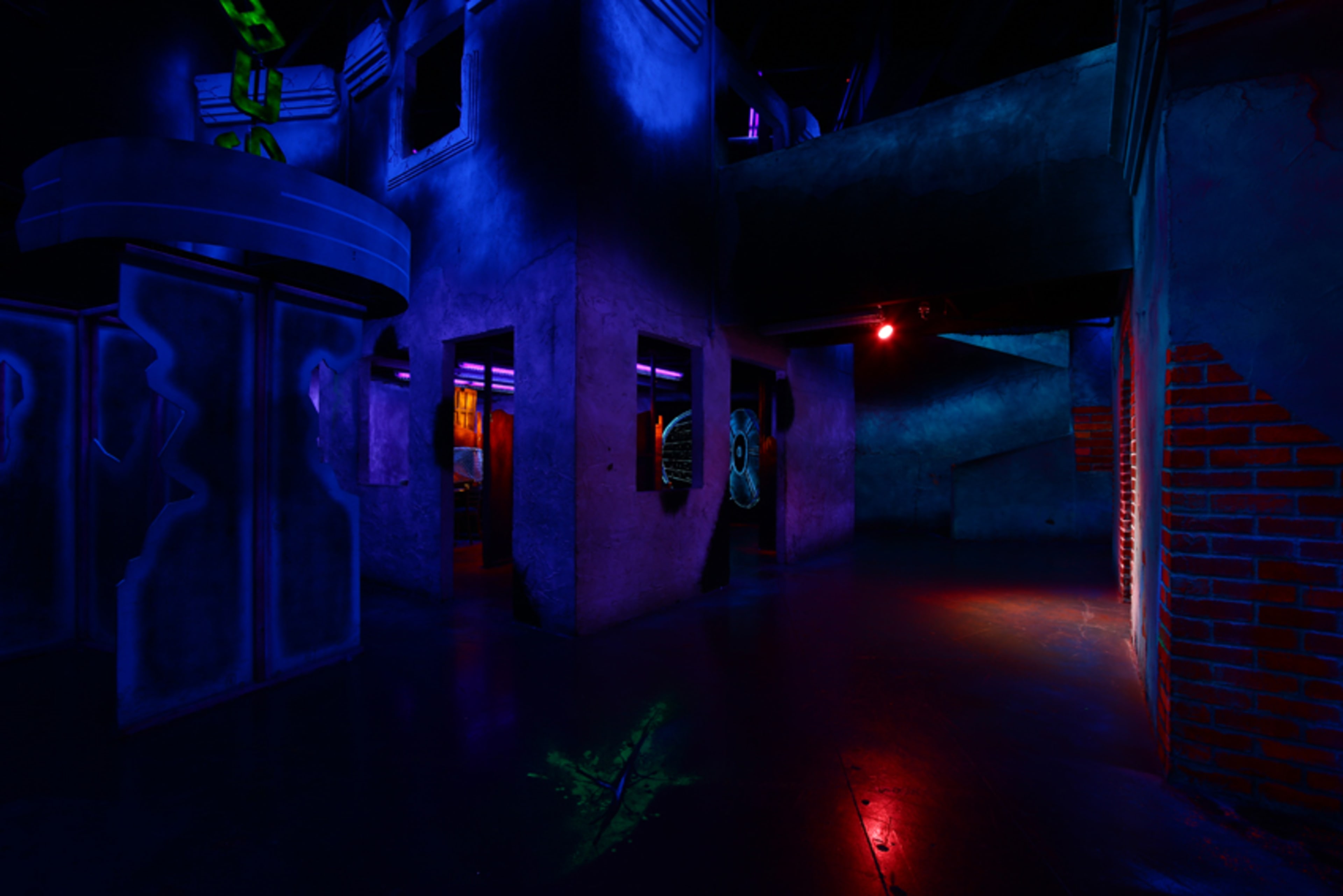 The image shows a dimly lit indoor space with dark walls and colorful lighting, featuring architectural structures and a visible entrance.