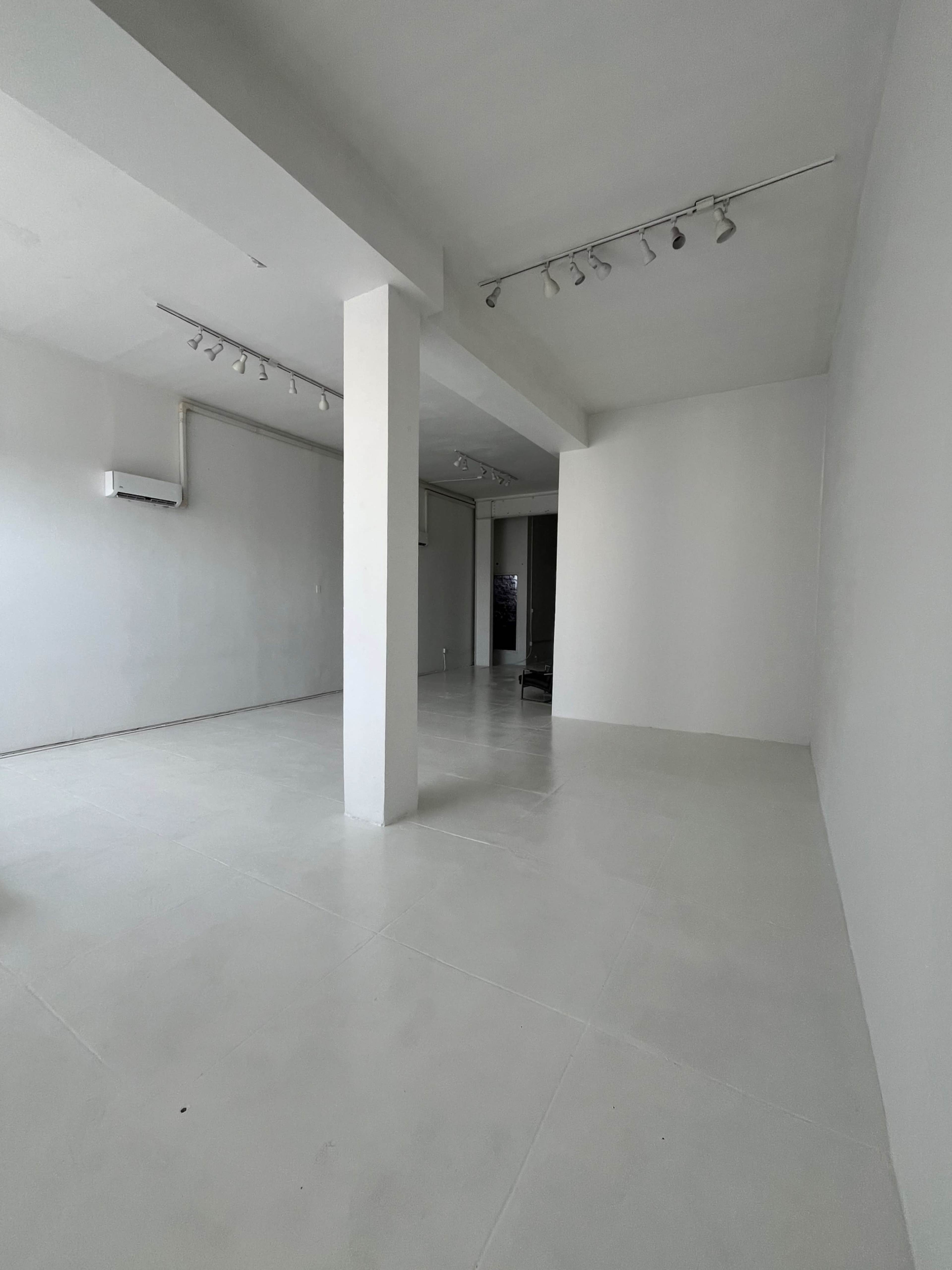The image shows a minimalist empty room with white walls and a tiled floor, featuring recessed lighting and an air conditioning unit.