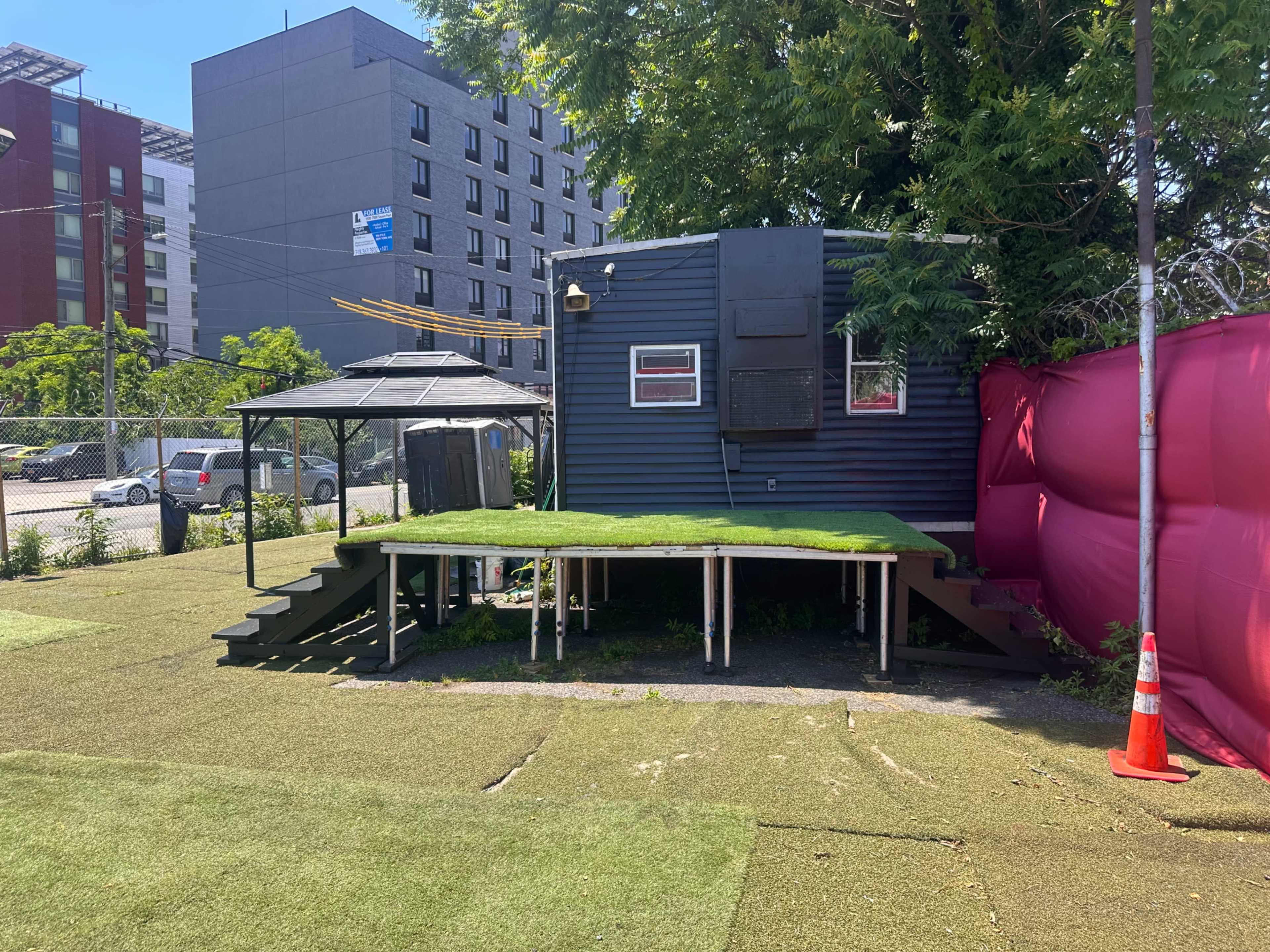 A small mobile structure with a green turf deck is situated next to a pink wall in an outdoor area.