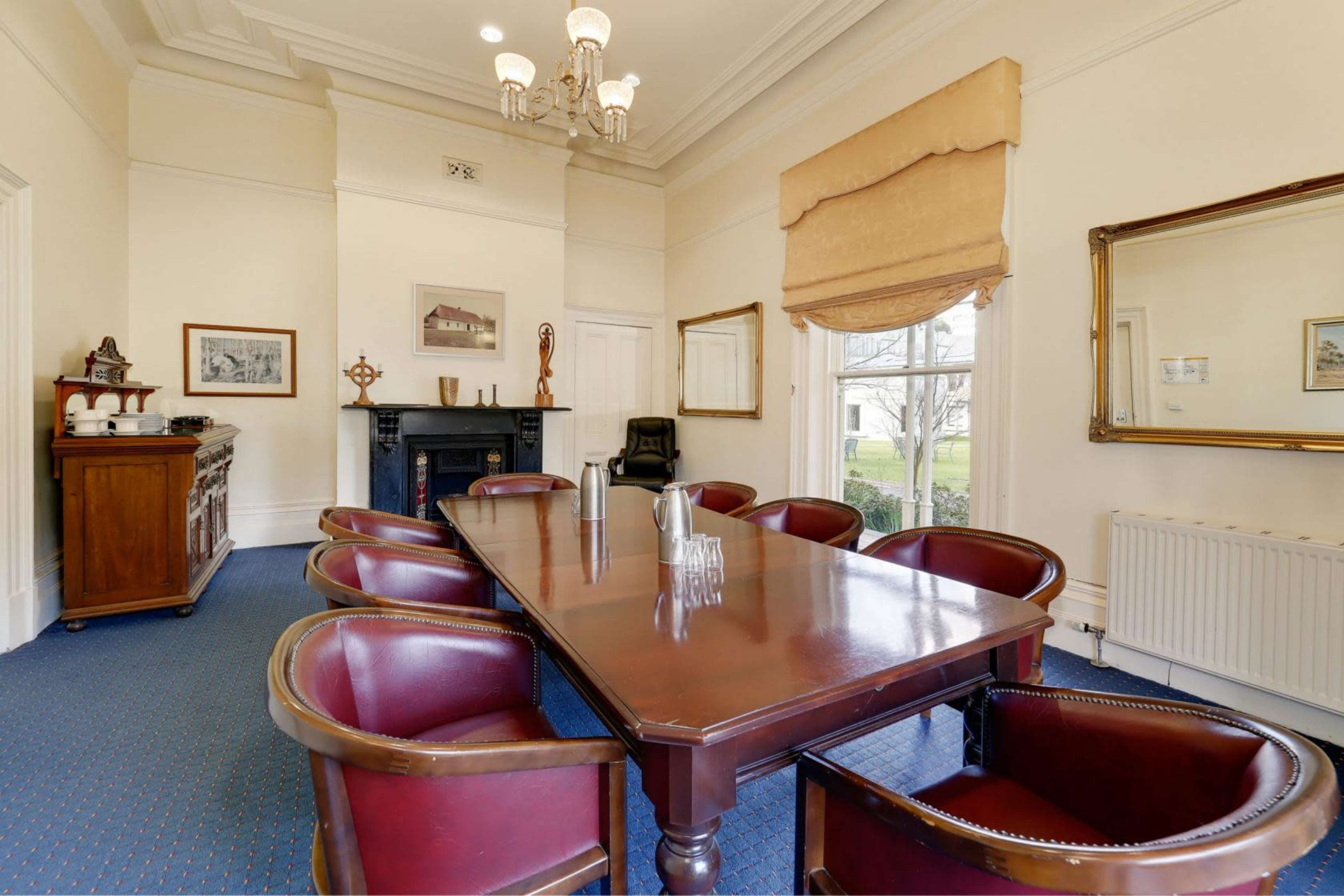 A dining room features a large wooden table surrounded by dark leather chairs, with a sideboard and a decorative mirror on the walls.