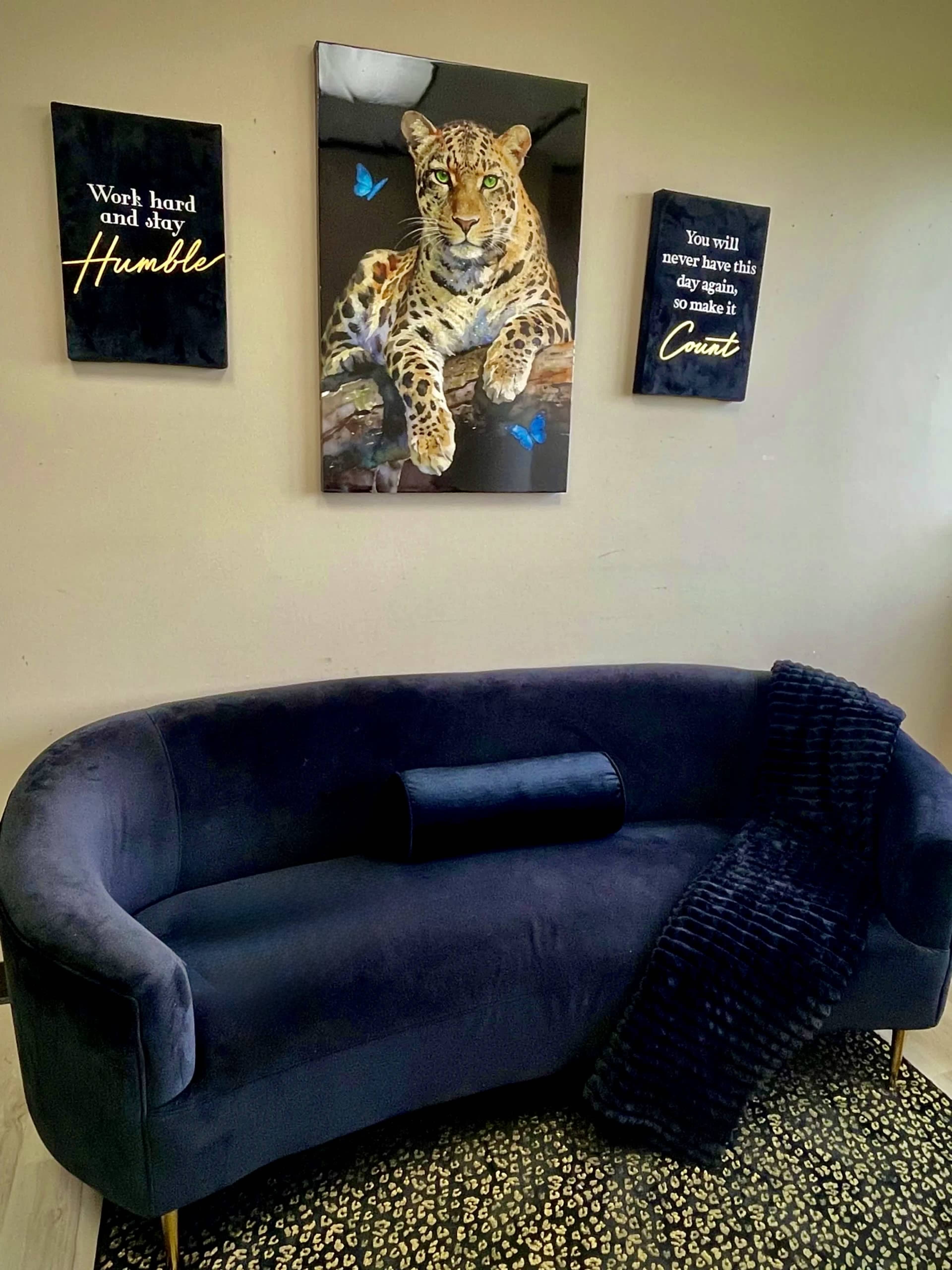 A navy blue velvet sofa is positioned against a plain wall adorned with three motivational wall art pieces, including a large framed image of a leopard surrounded by butterflies.