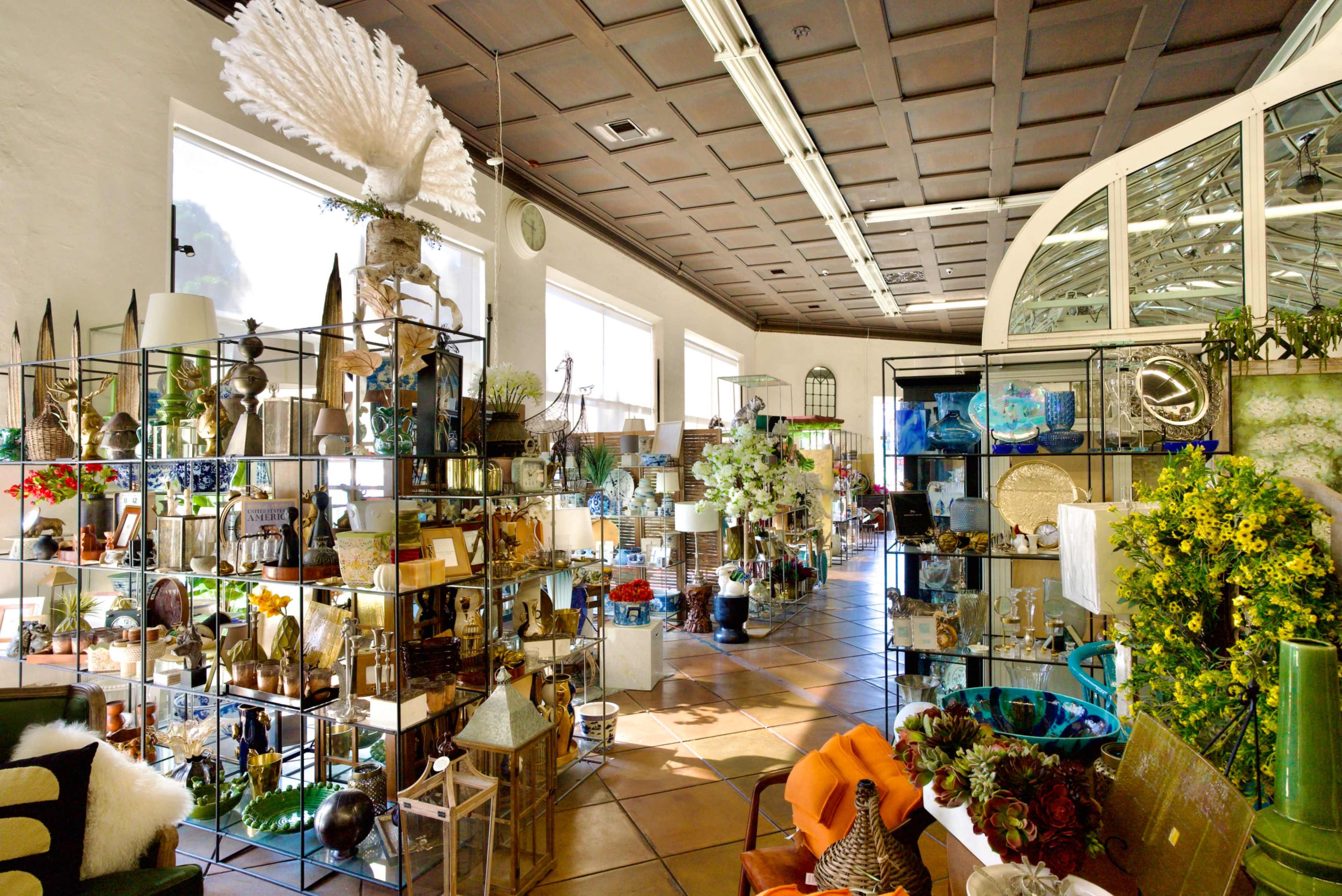 The image shows a brightly lit interior of a home decor store featuring various decorative items arranged on metal display shelves.