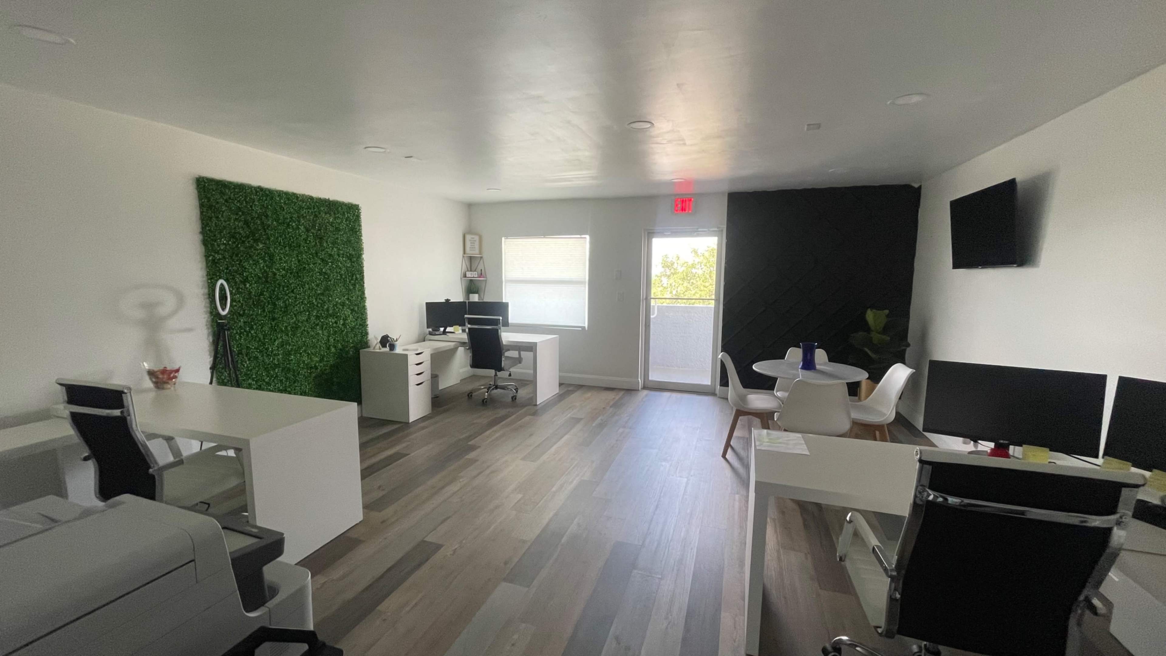 A modern office space with multiple desks, a printer, and a green accent wall.