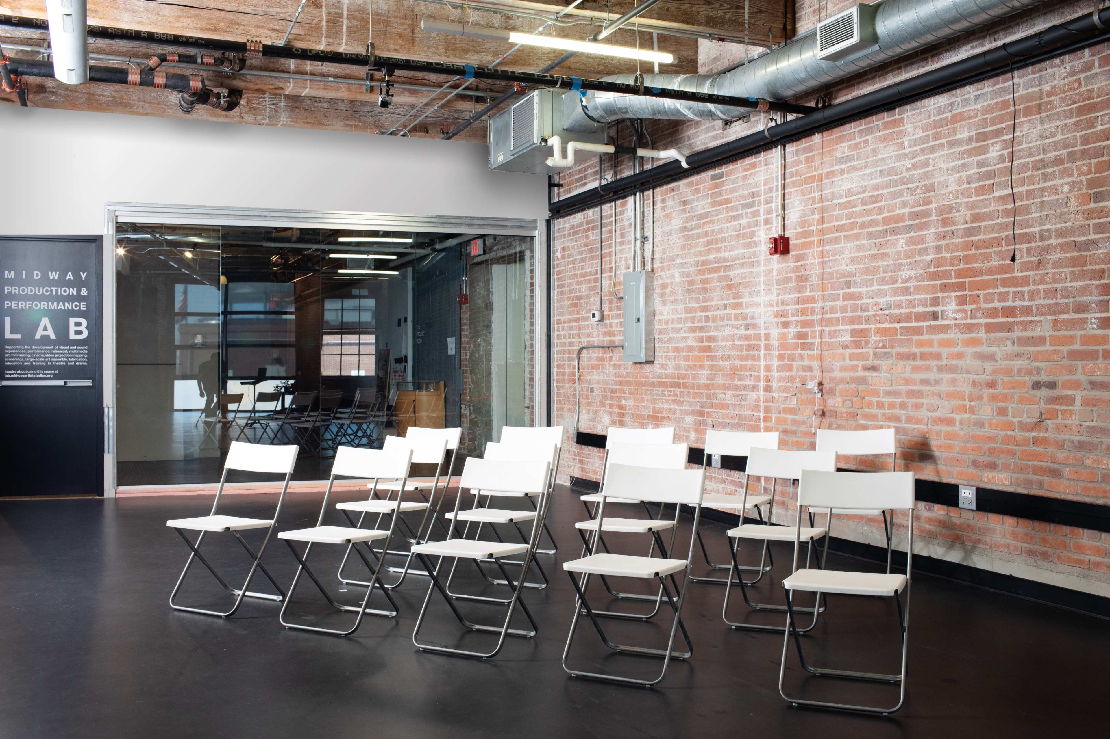 A row of metal and plastic folding chairs is arranged in a space with exposed brick walls and industrial-style features.