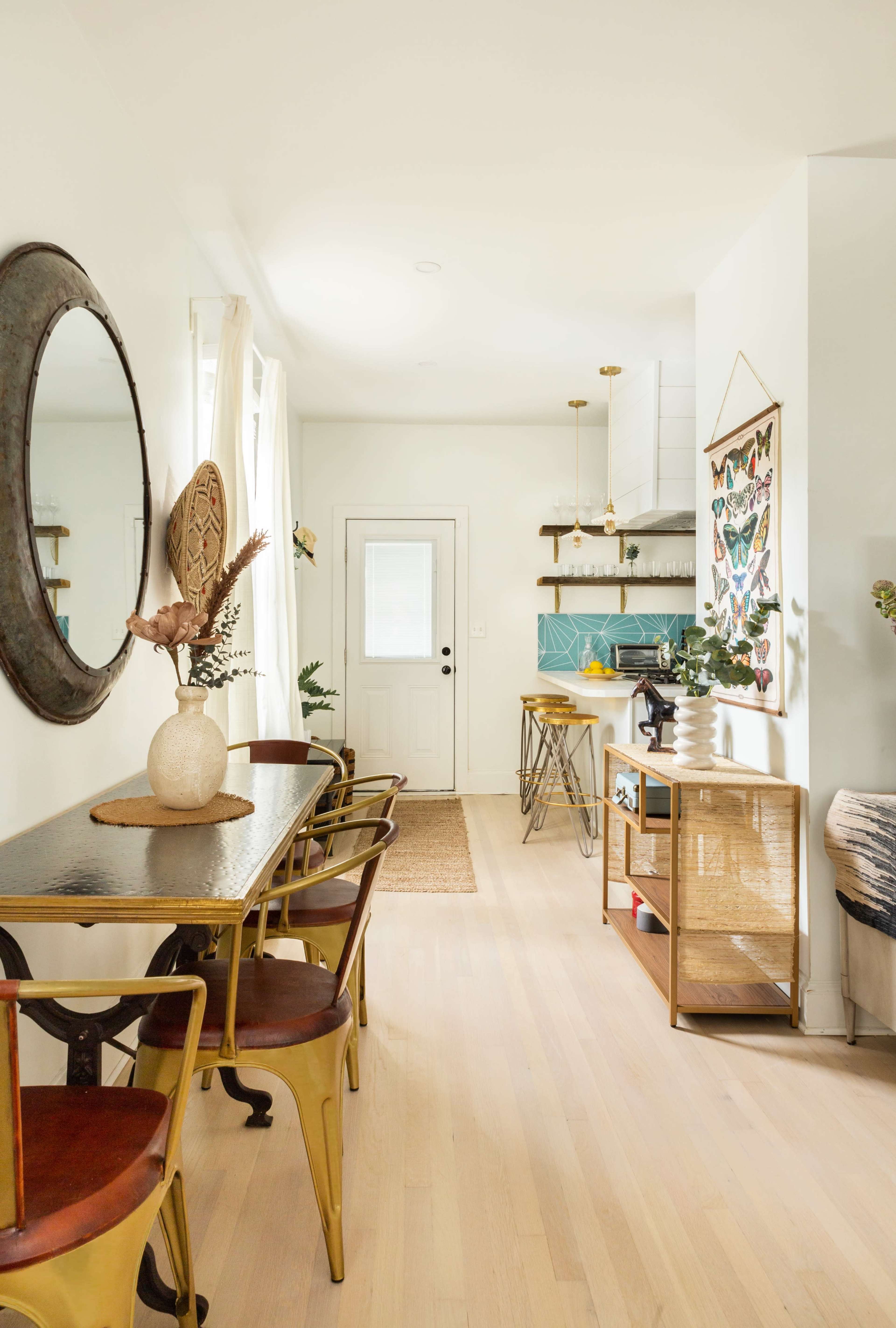 A bright dining area featuring a round table with metal chairs, a light-colored wooden floor, and a door leading to an outside space.