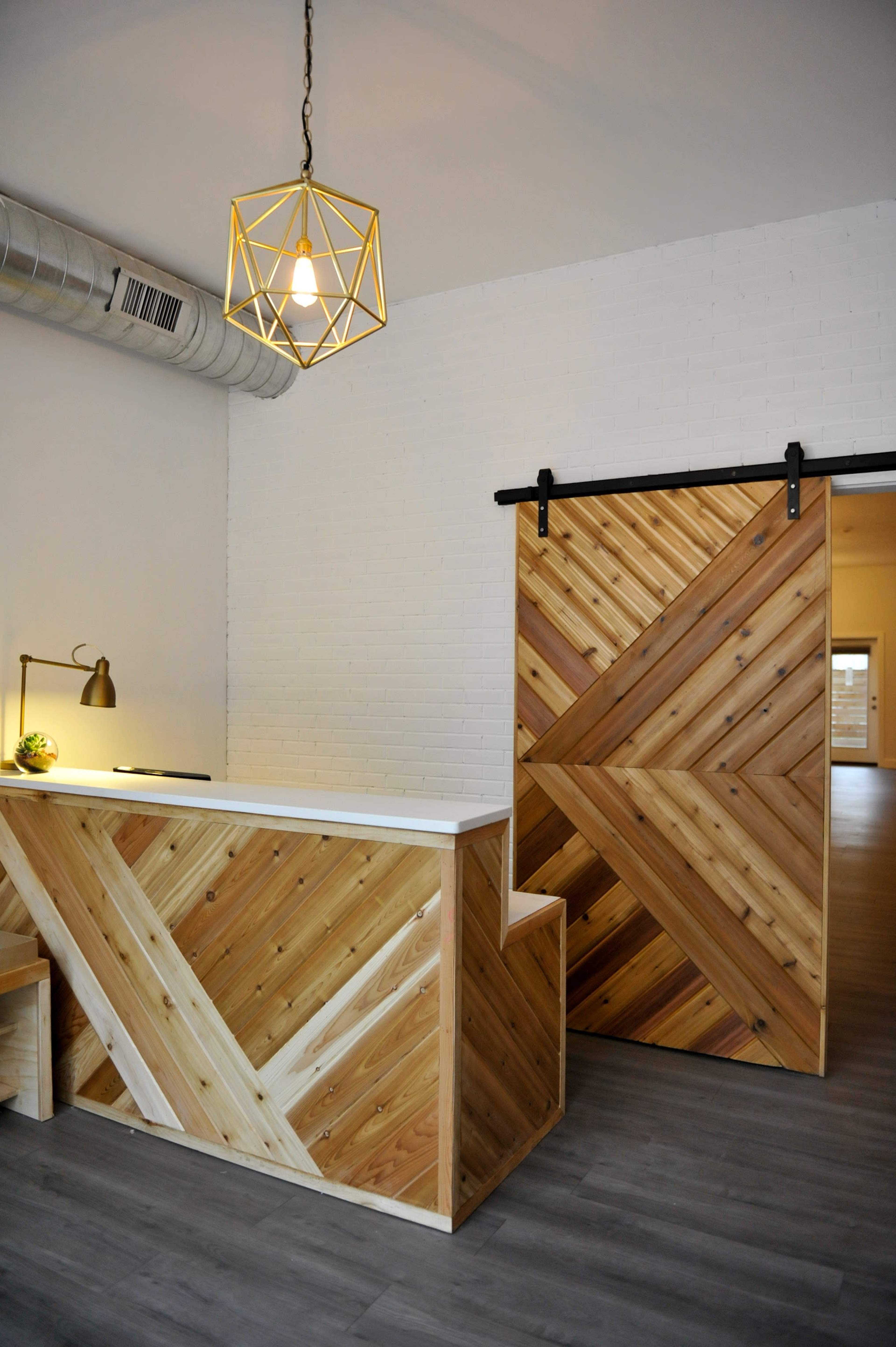 The image shows a modern reception area featuring a wooden reception desk with a chevron pattern and a sliding barn door made of similar wood.