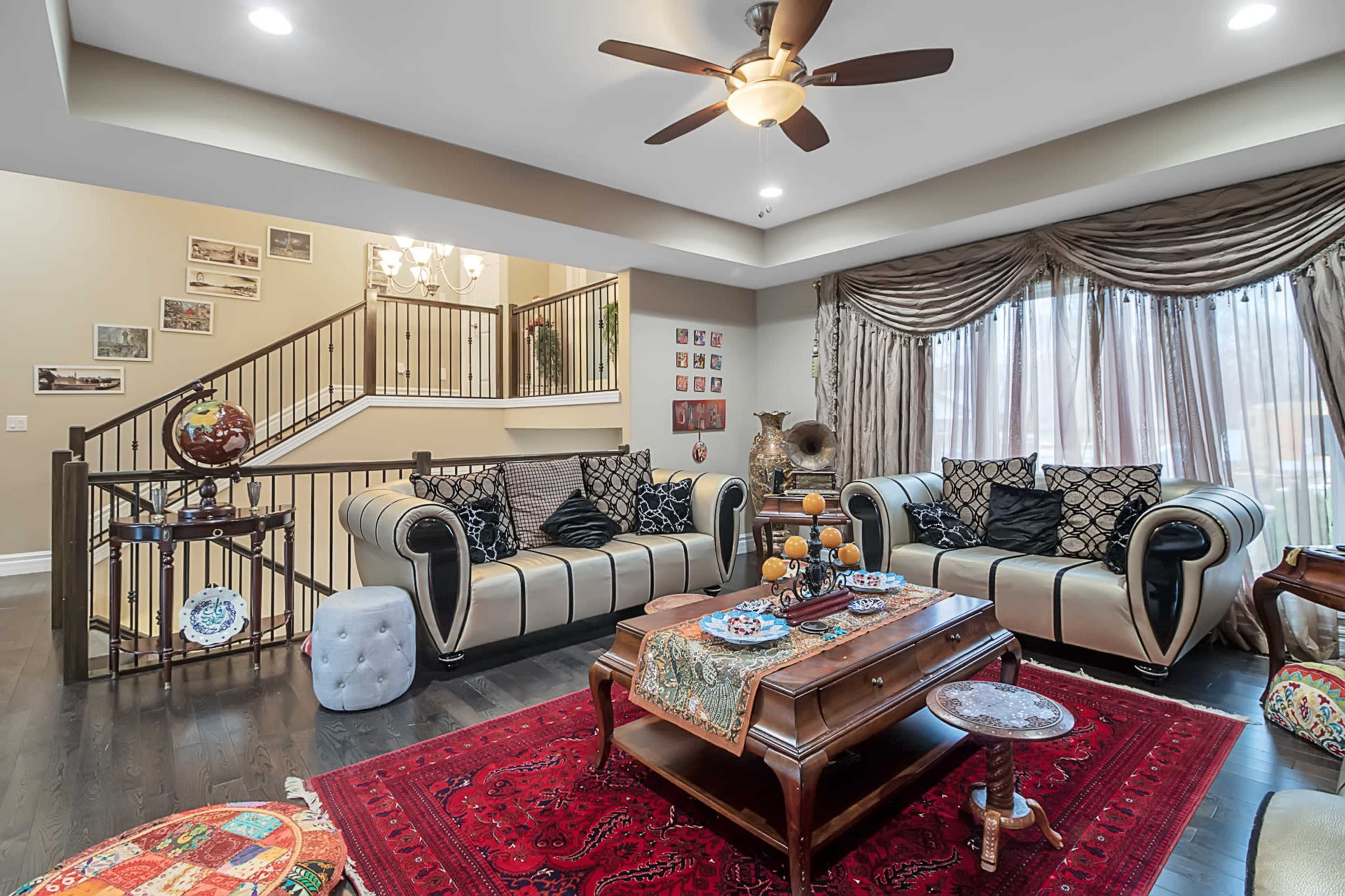 The living room features two plush sofas patterned in black and white, a wooden coffee table adorned with decorative items, and a large window draped with elegant curtains.