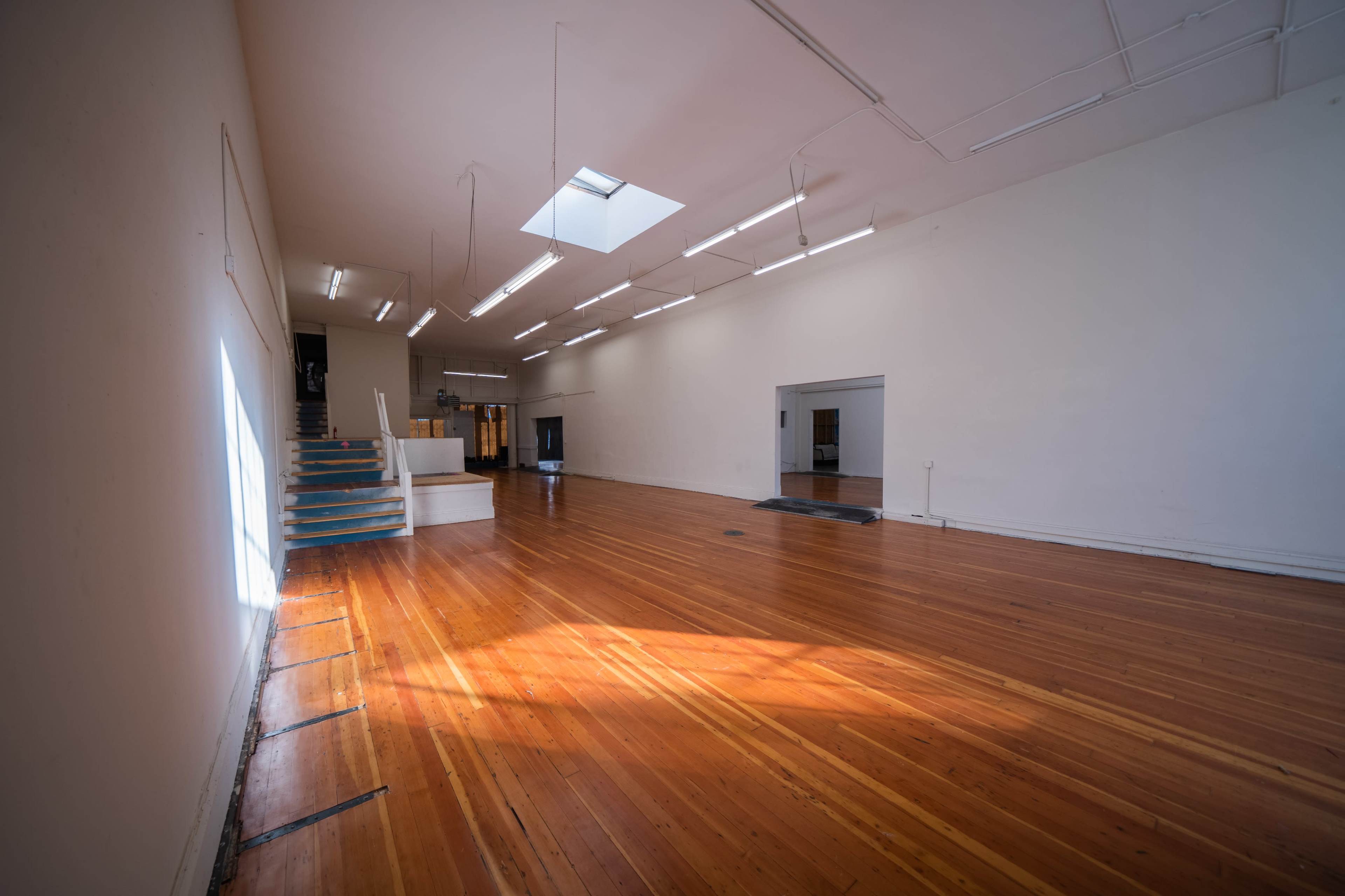 A large, empty interior space with polished wooden floors, white walls, and skylights illuminating the area.