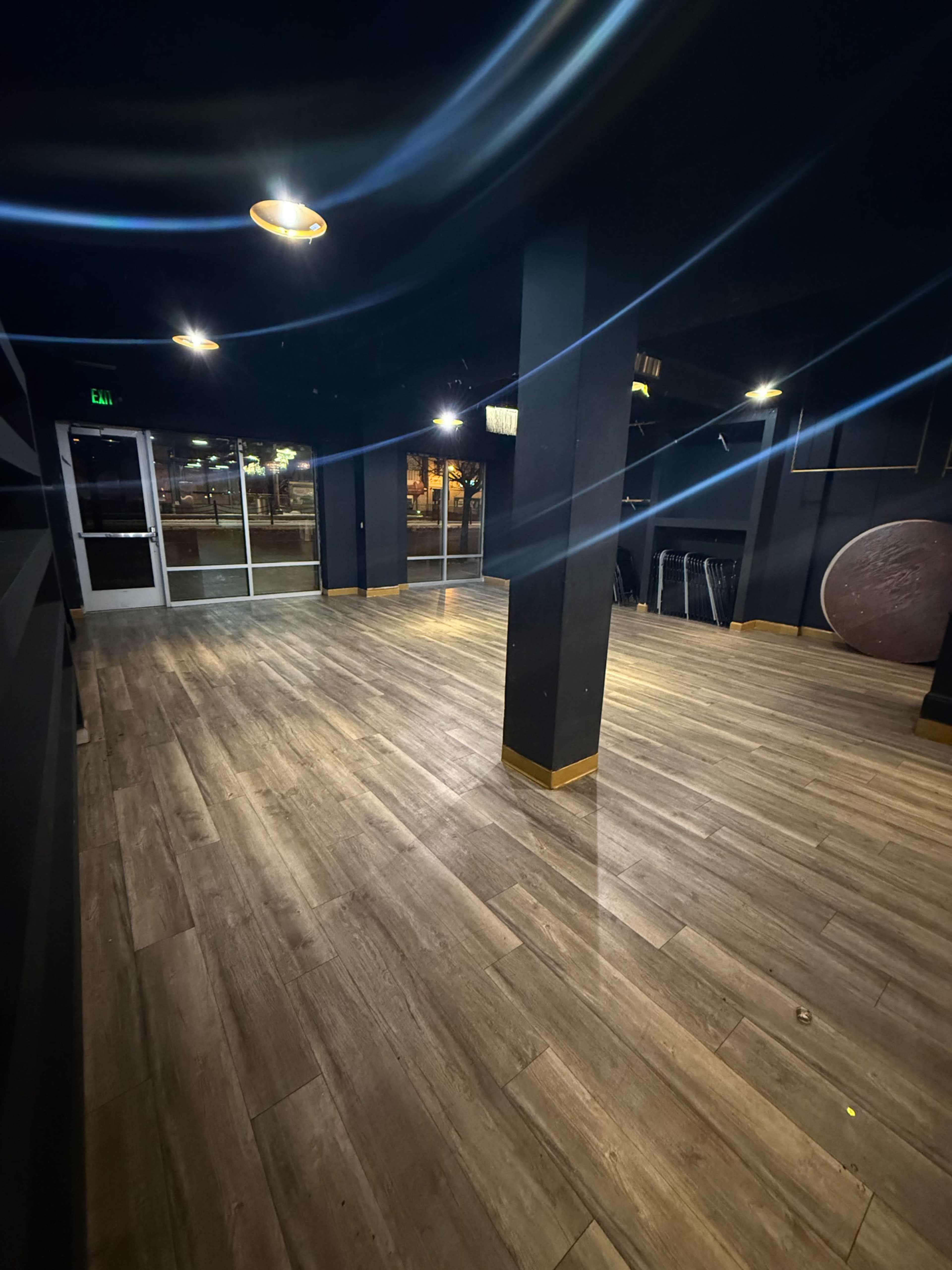 The image shows an empty room with wooden flooring, black walls, and several light fixtures illuminating the space.