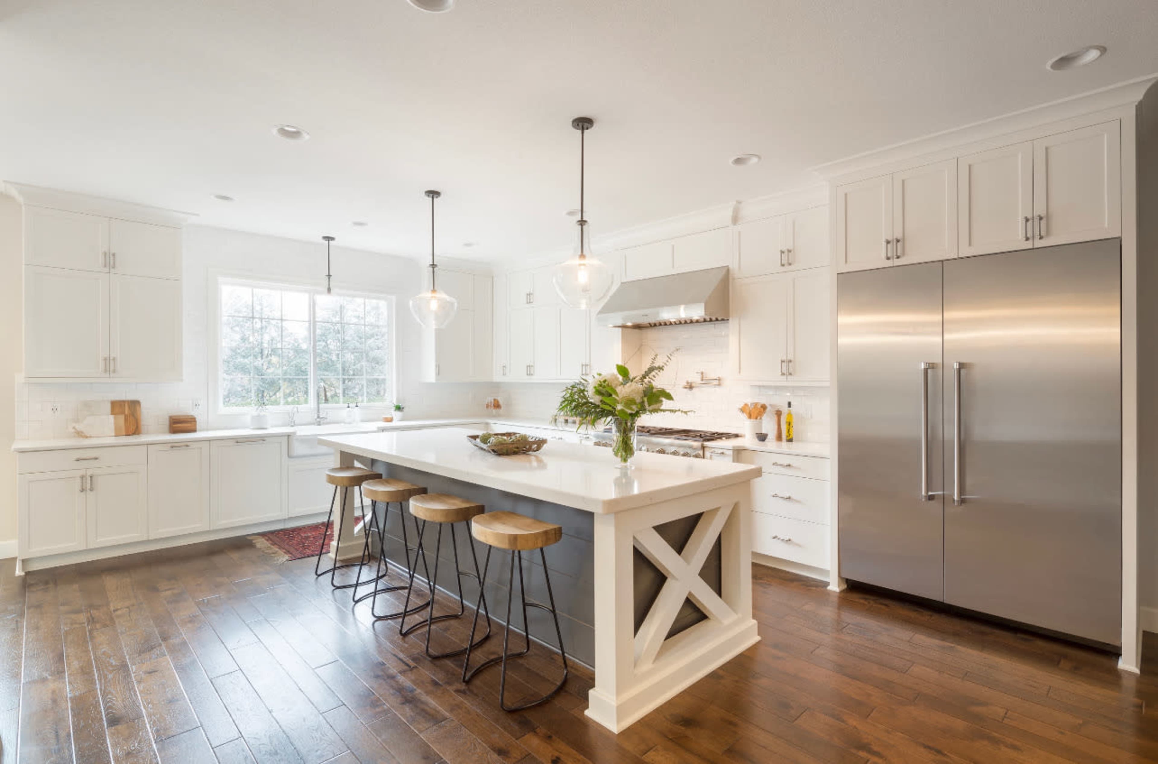 The image shows a modern kitchen featuring white cabinetry, a large central island with bar stools, and stainless steel appliances.