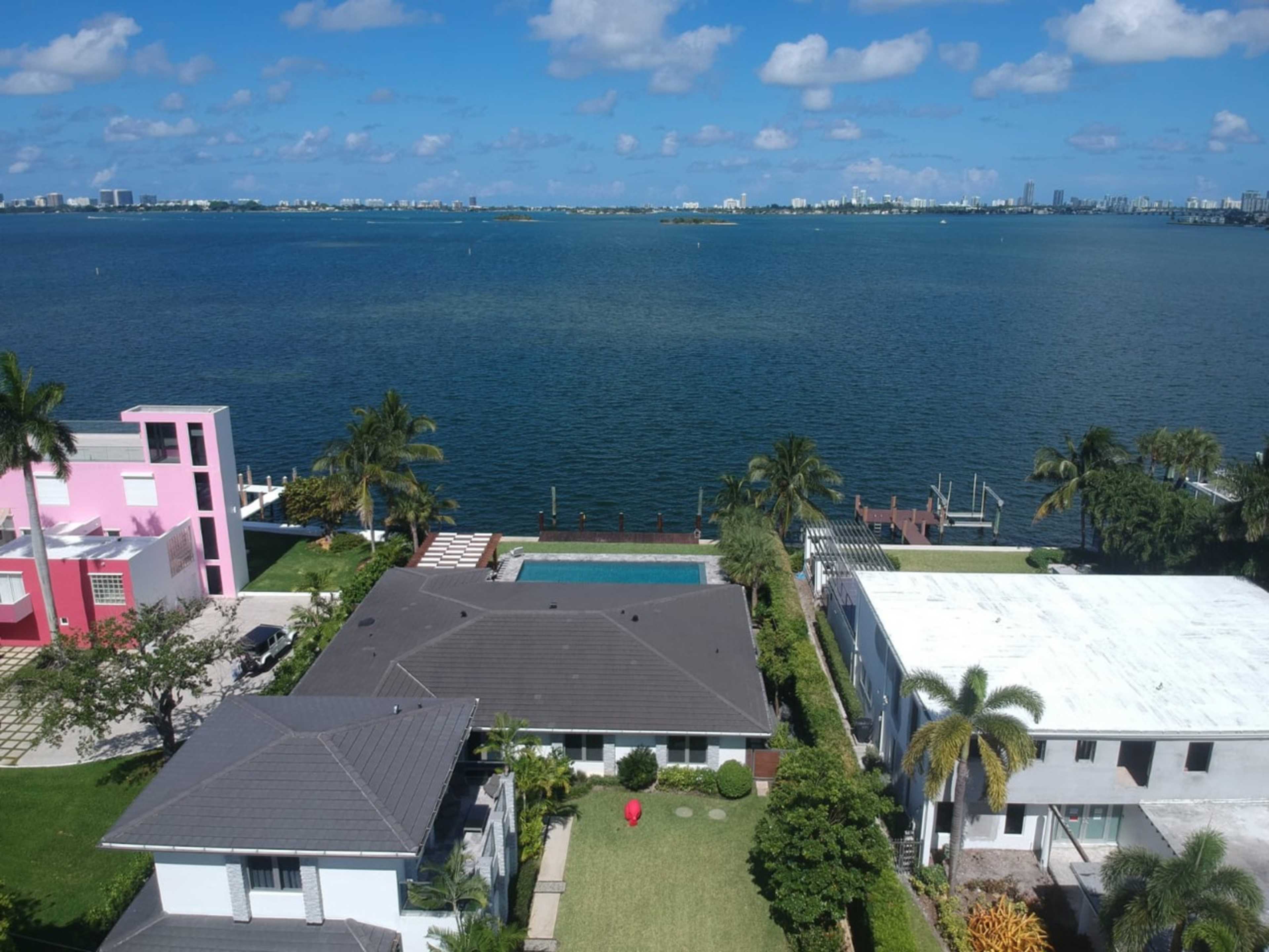 The image shows a waterfront residential area with several houses, a swimming pool, and a view of the water and distant city skyline.