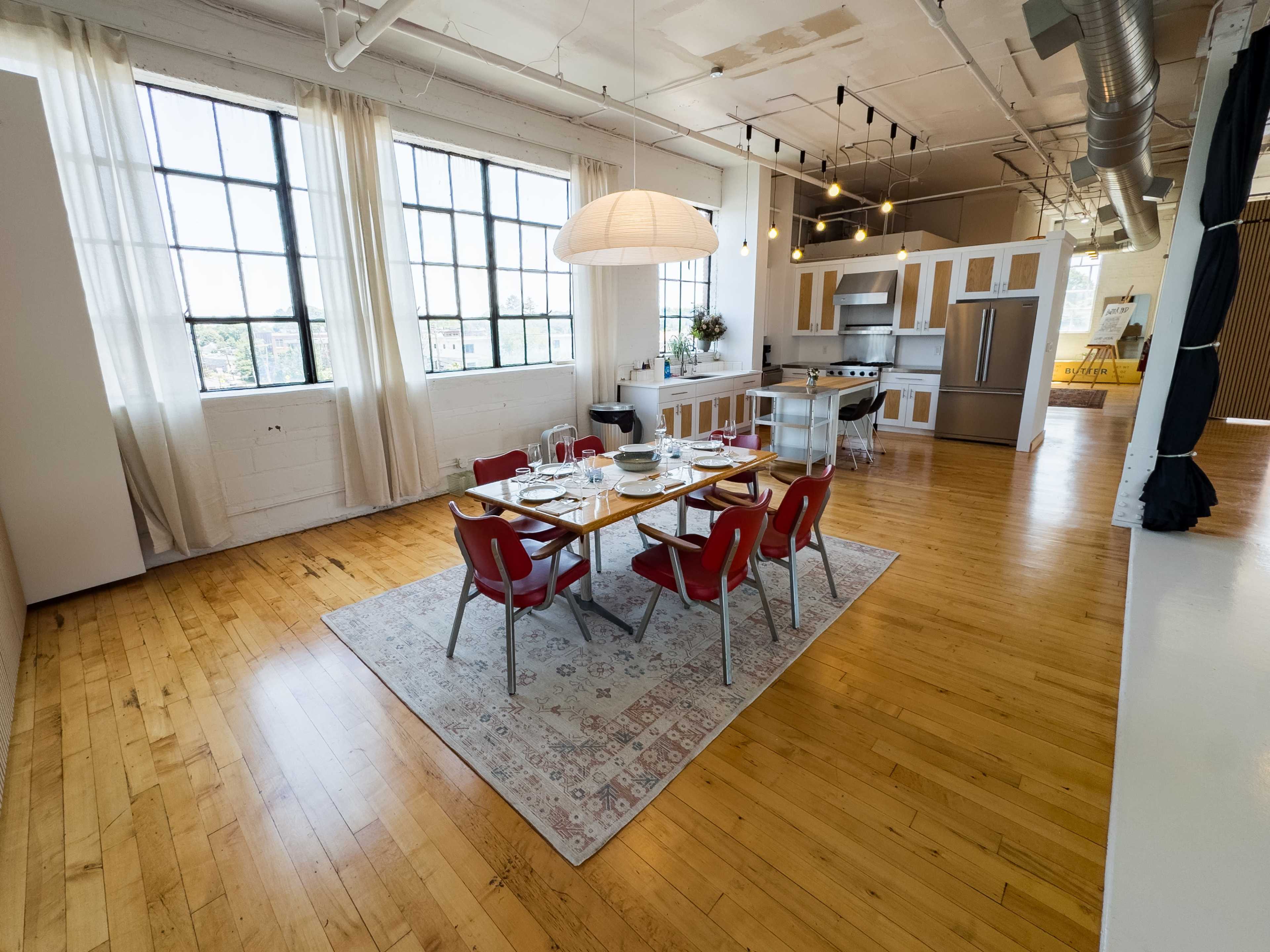 A spacious dining area with a wooden table set for a meal, surrounded by red chairs, and large windows providing natural light.