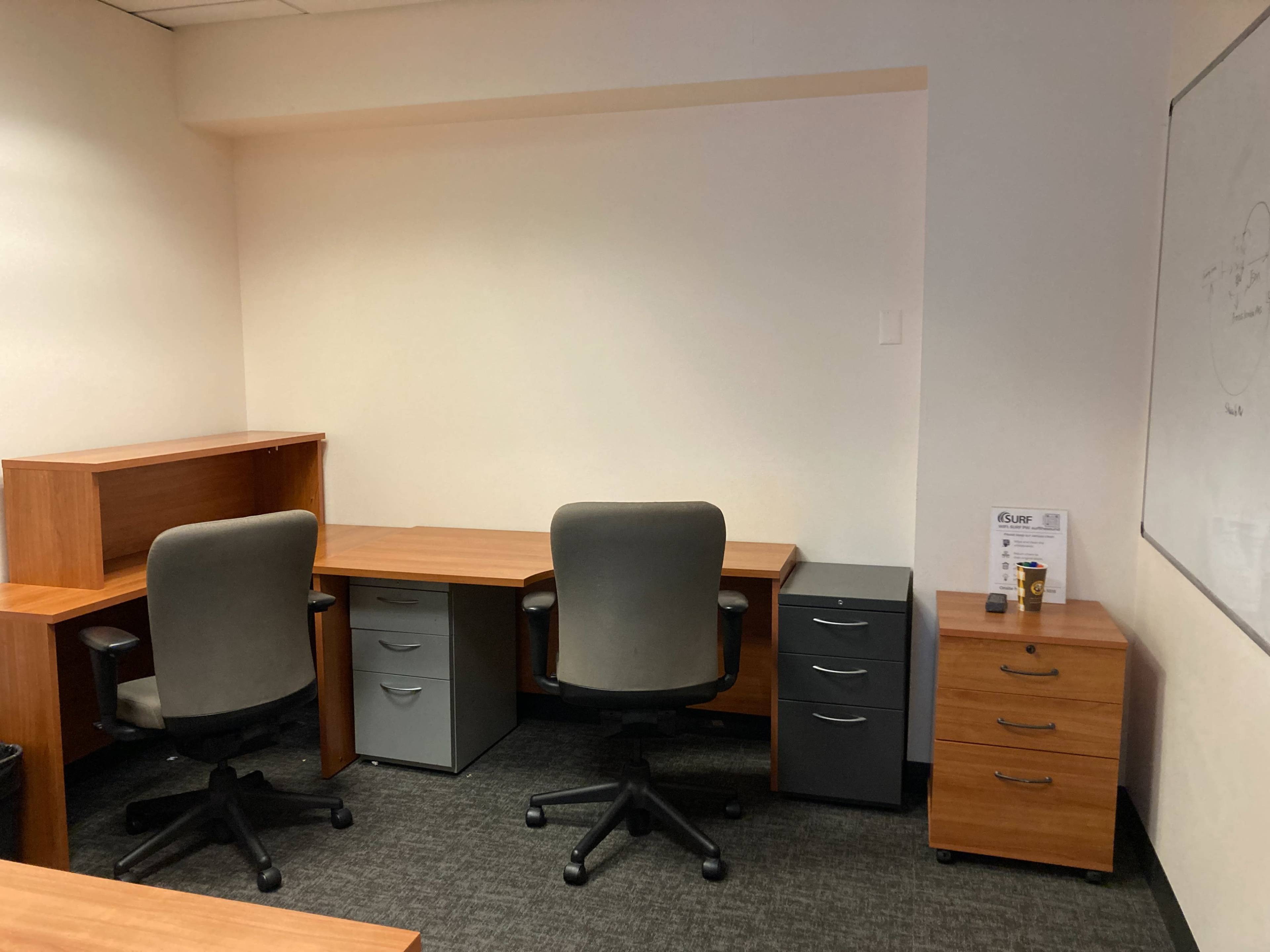 The image shows a minimalist office space with two desks, two office chairs, and several storage cabinets.
