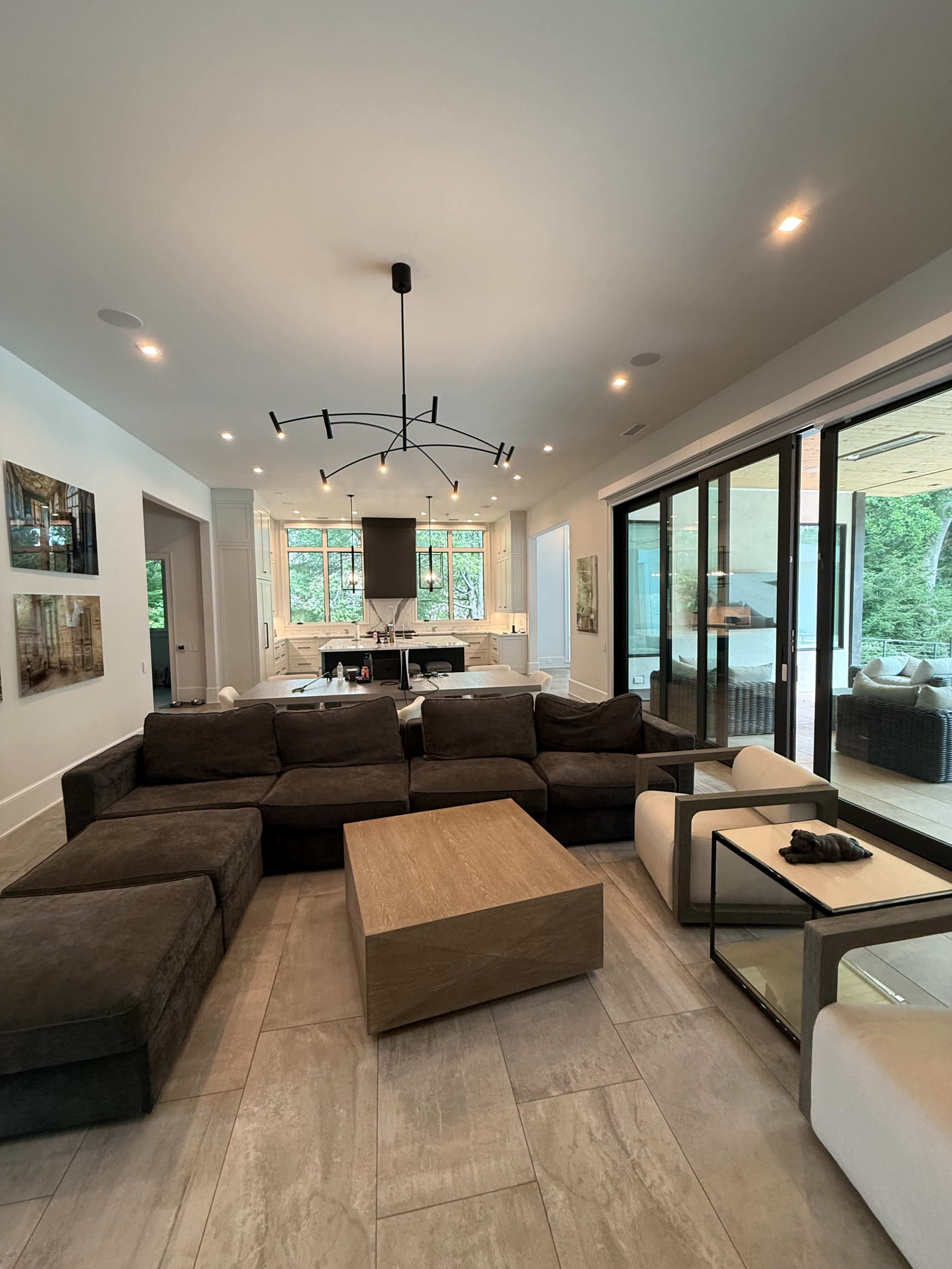 The image shows a modern living room featuring a sectional sofa, a wooden coffee table, and large glass doors leading to an outdoor area.