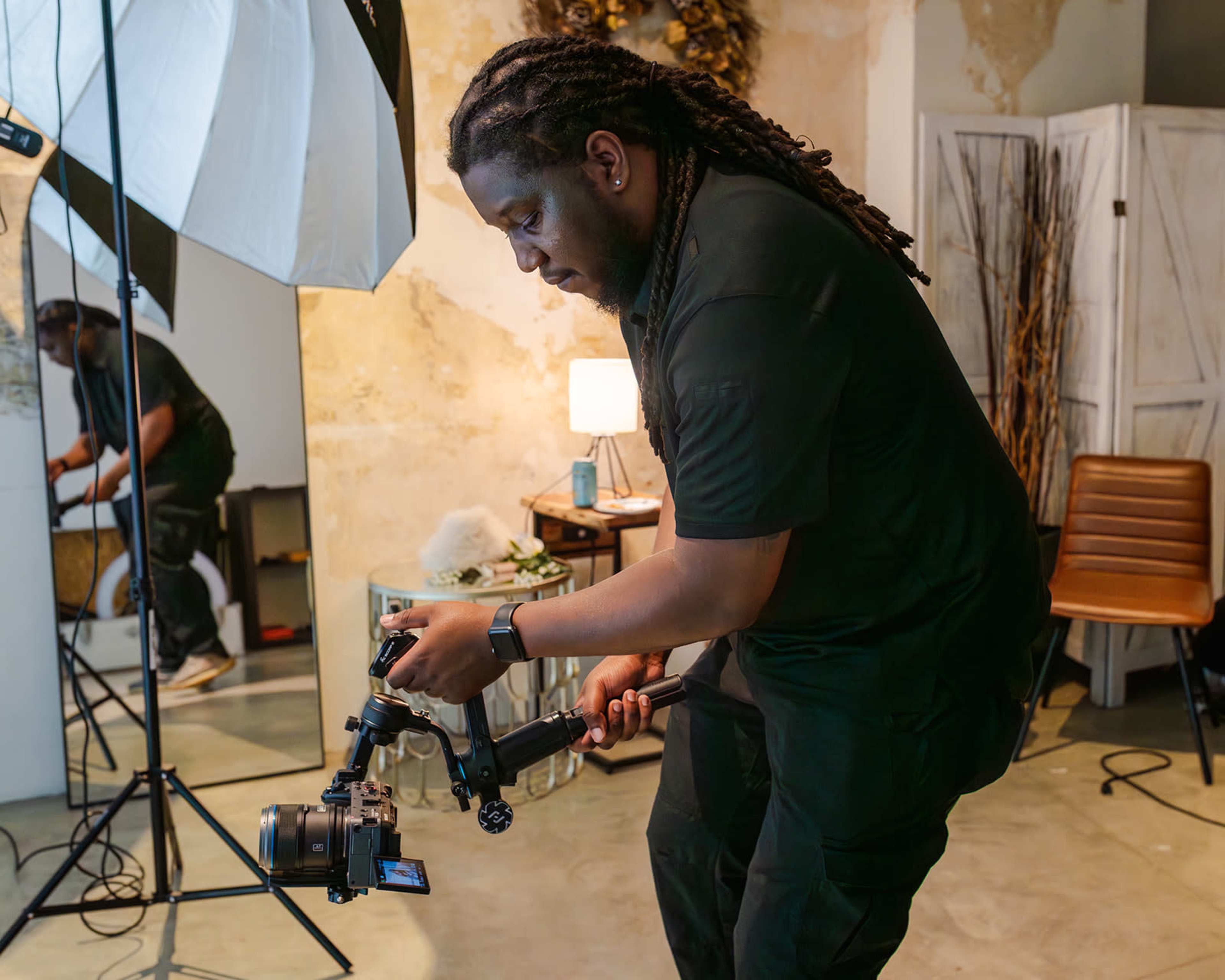 A man adjusts a camera on a gimbal in a studio setting with soft lighting and decorative elements in the background.